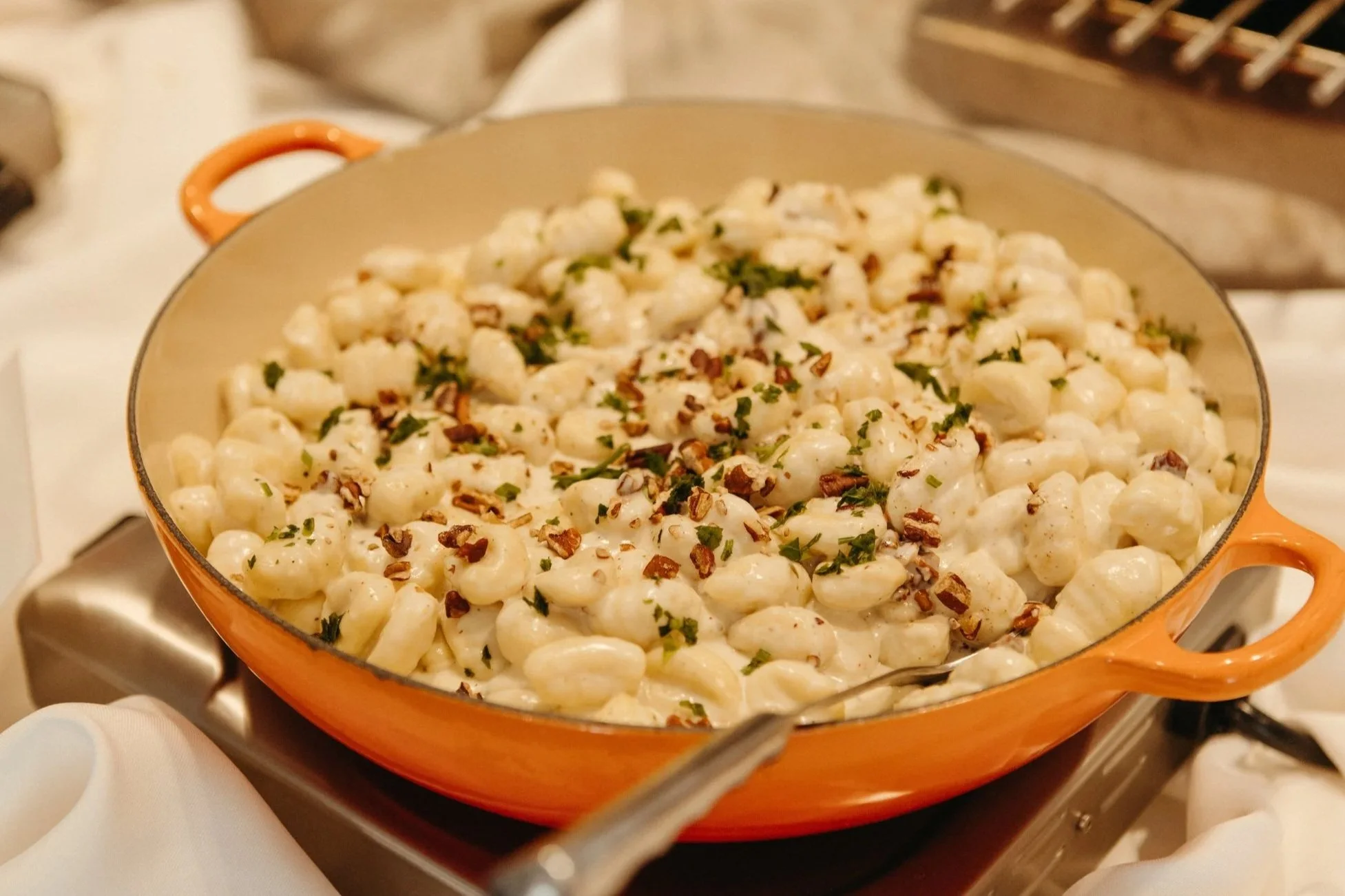 Creamy gnocchi with chopped herbs and toasted nuts in an orange pan.