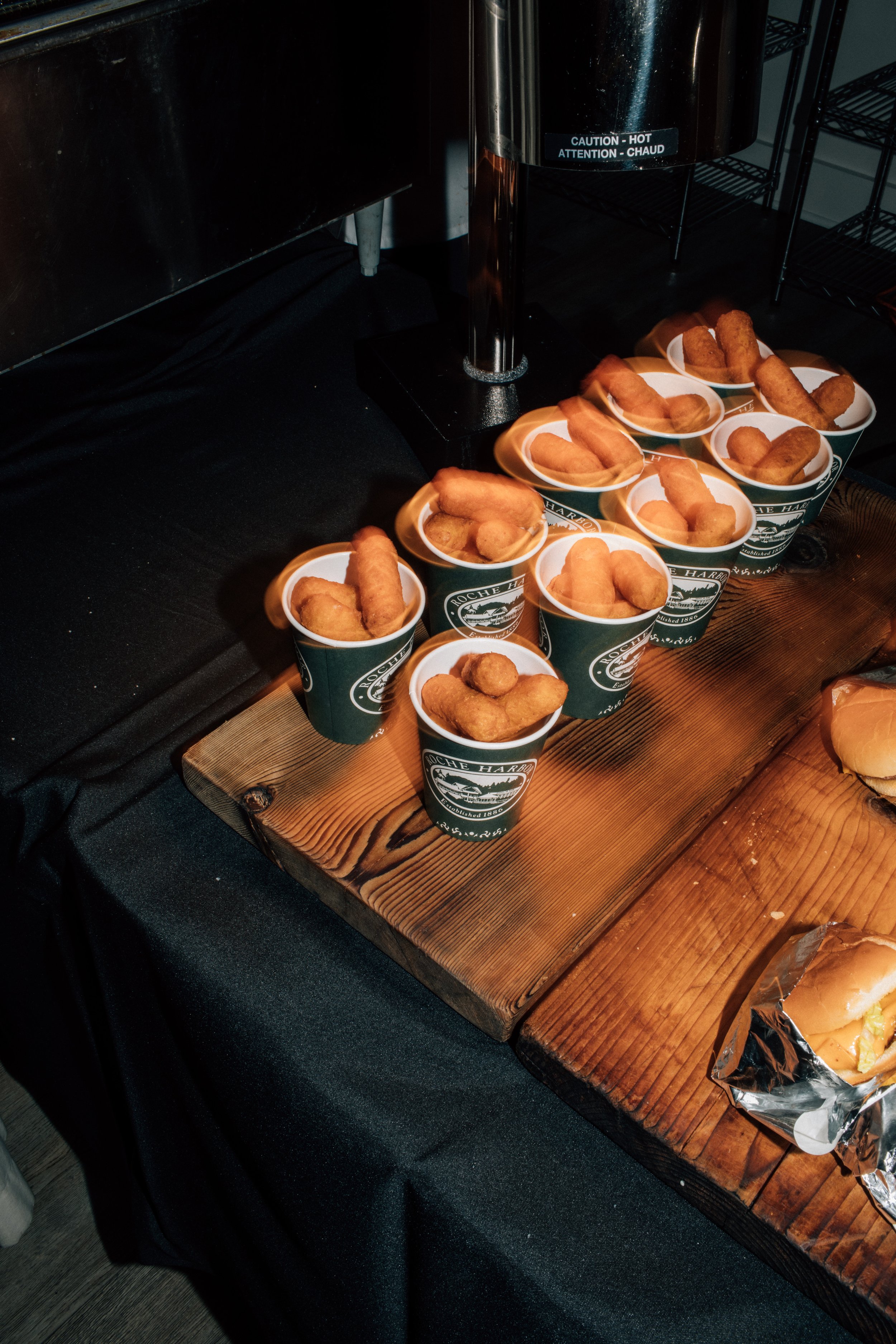 Multiple cups of fried fish sticks or chicken tenders in dark green paper cups on a wooden display at a food station or buffet.