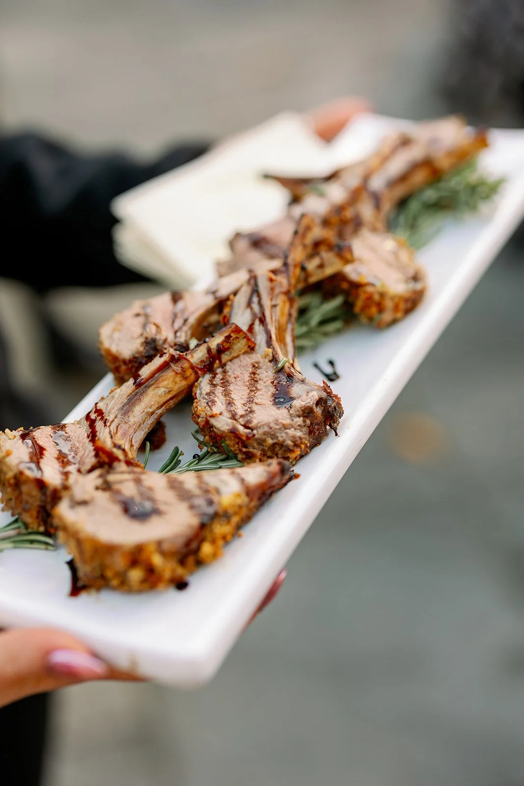 Grilled lamb chops with a side of cheese, seen on a white rectangular plate garnished with herbs.