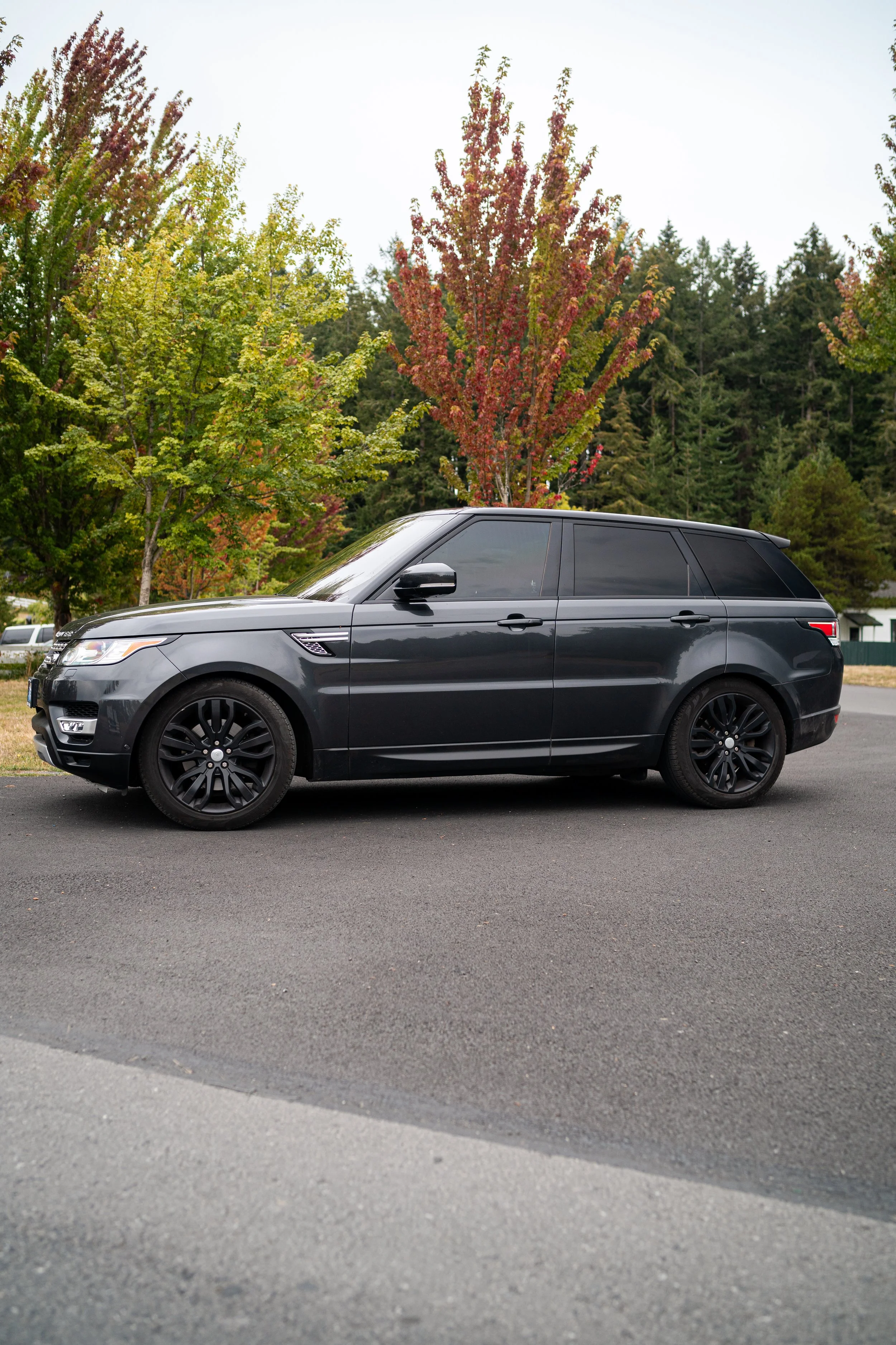 A black SUV parked on a paved road with trees in autumn foliage in the background.