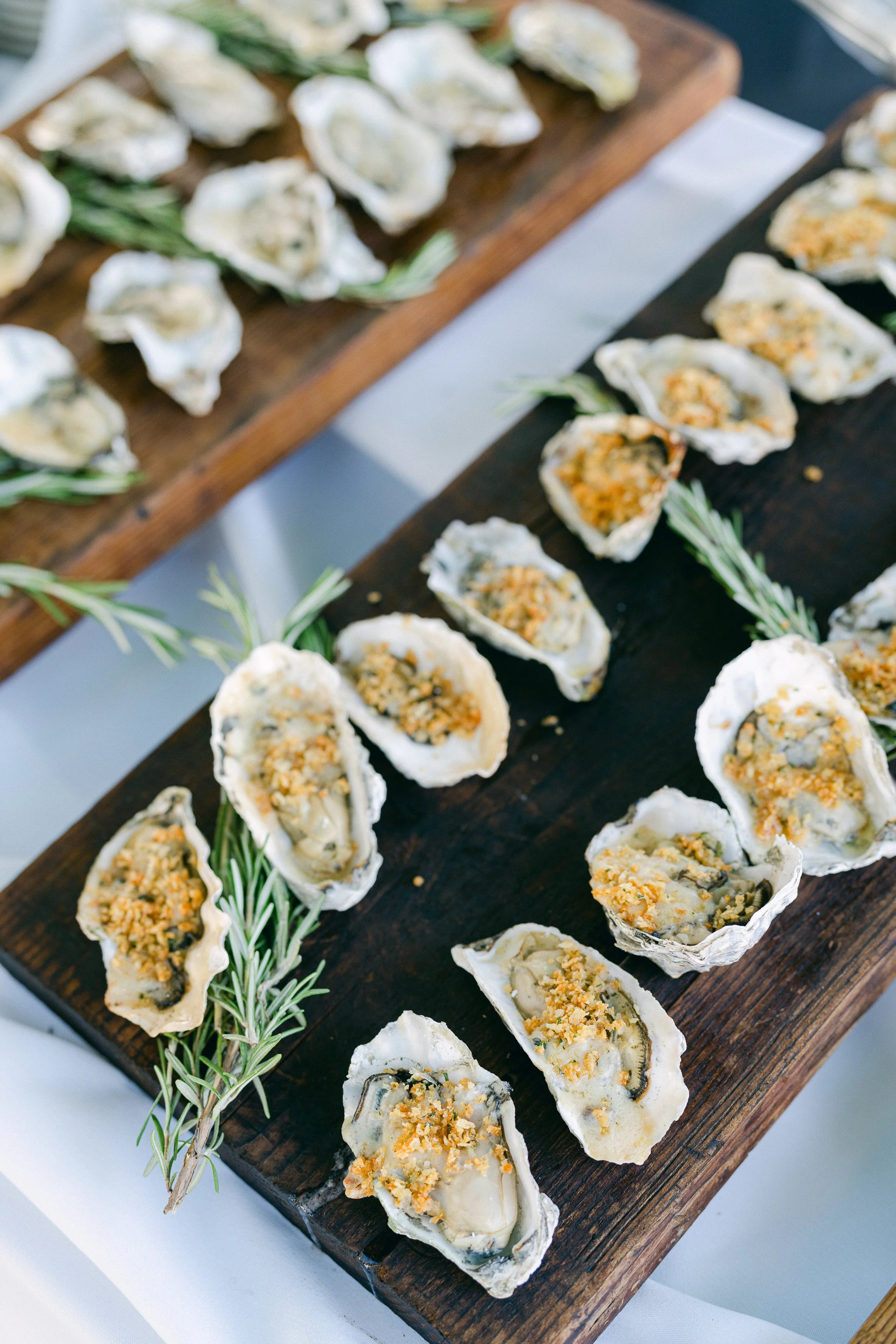 Oysters on a dark wooden serving board garnished with sprigs of rosemary.