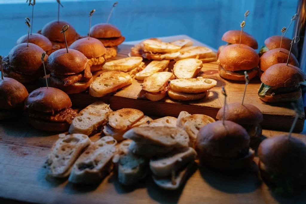 Assorted sliders and sandwiches on a wooden platter with toothpicks.