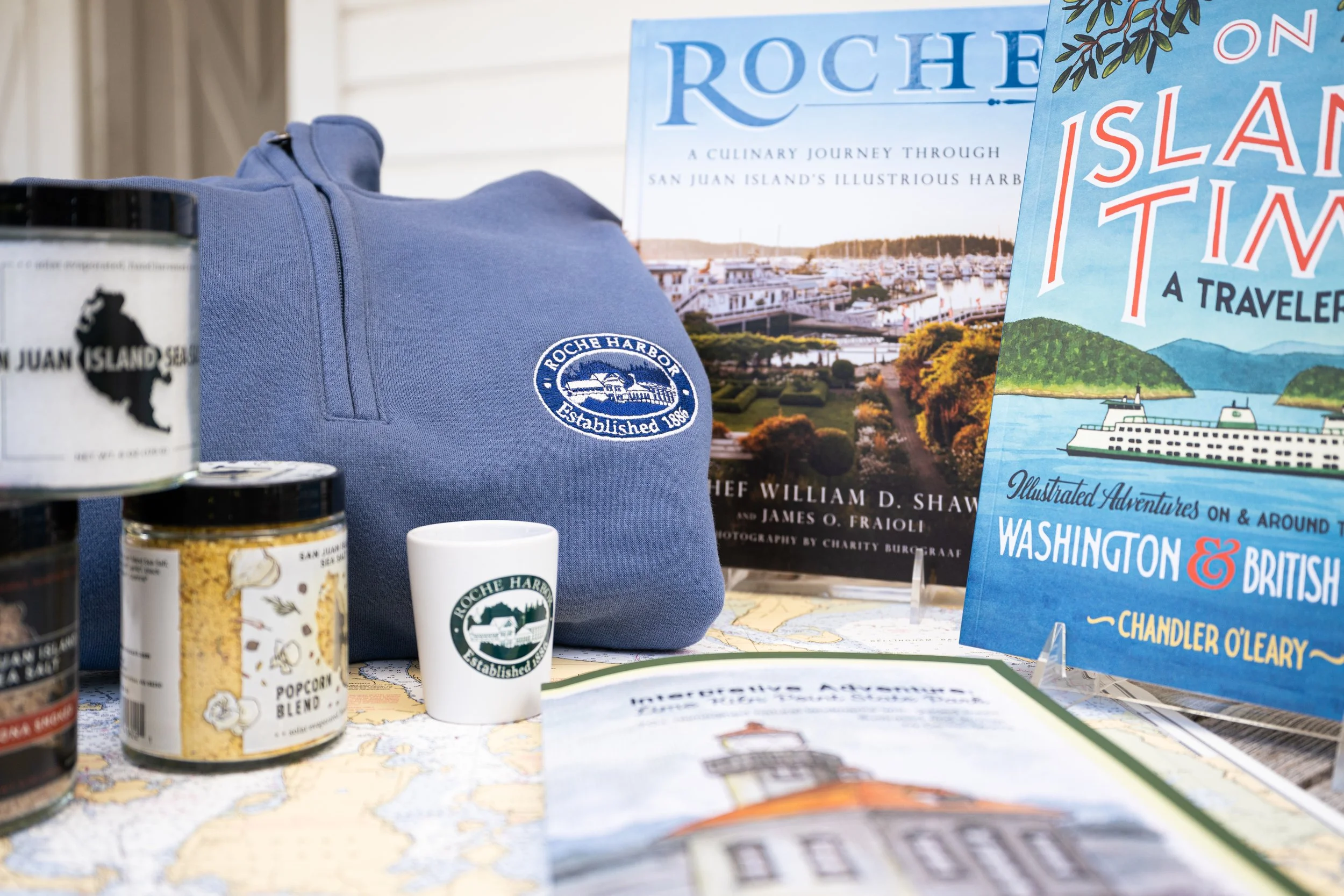 Items promoting Roche Harbor and San Juan Island, including a blue sweatshirt with a logo, a mug, a packet of popcorn blend, books about the island and cruises, and a map.