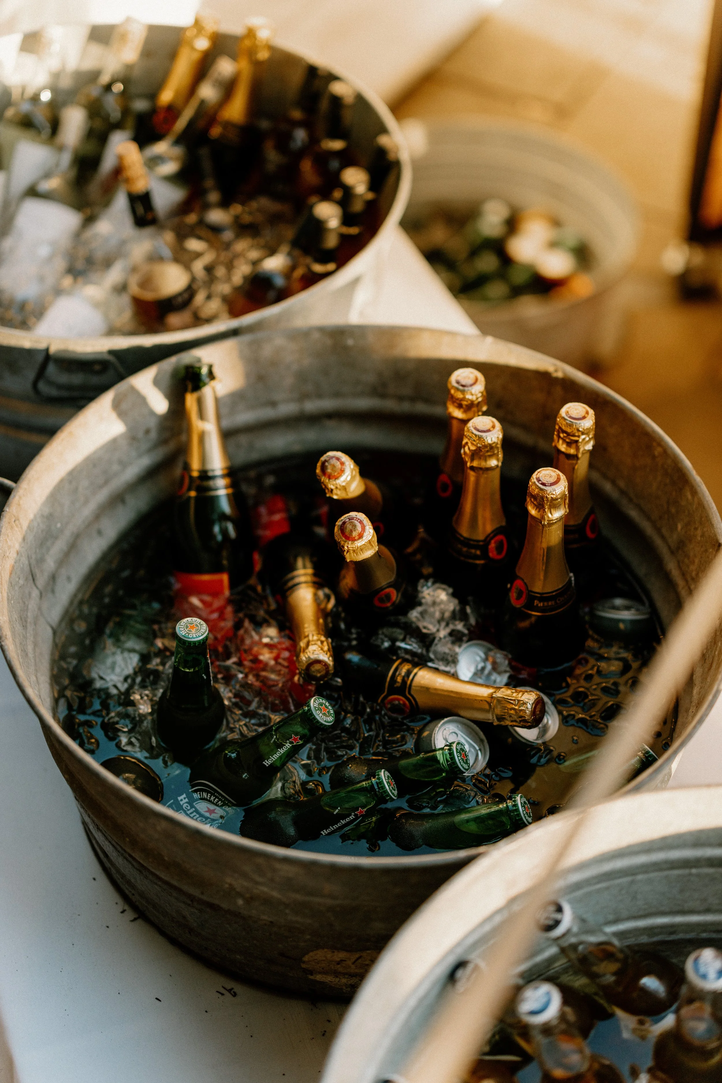 Bottles of beer chilling in metal tubs filled with ice at a gathering or party.