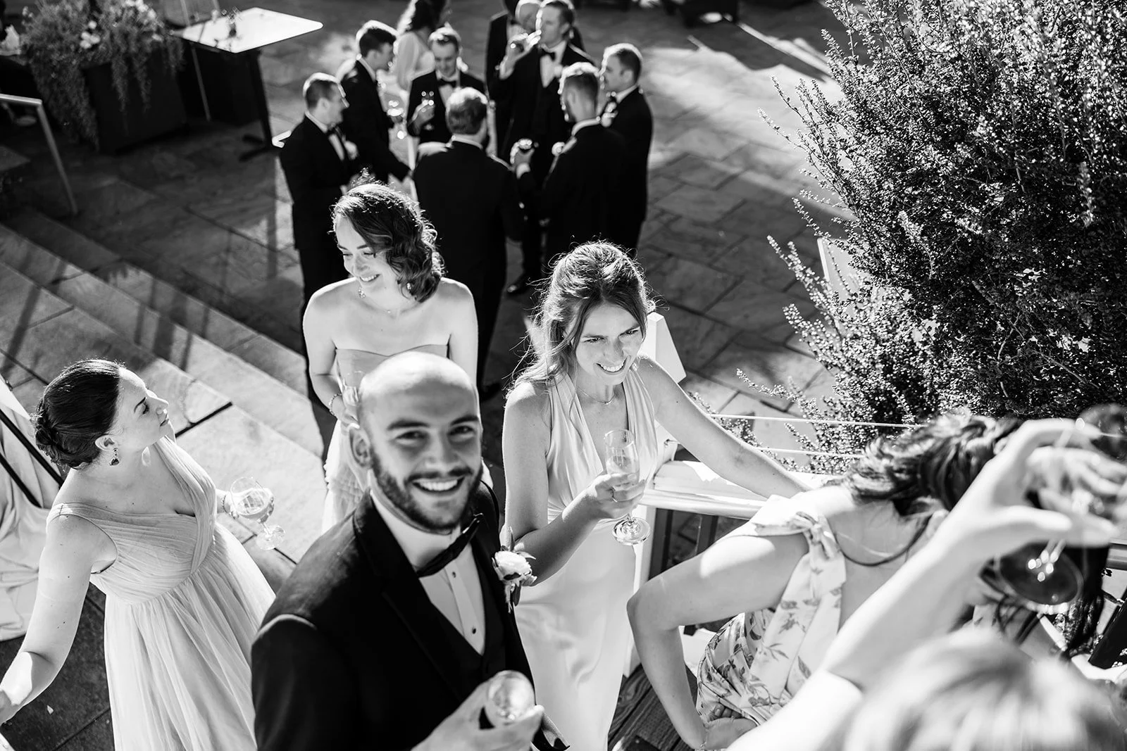 Guests enjoying a wedding reception, standing on a staircase and patio, holding glasses of champagne, dressed in formal attire, smiling and socializing.