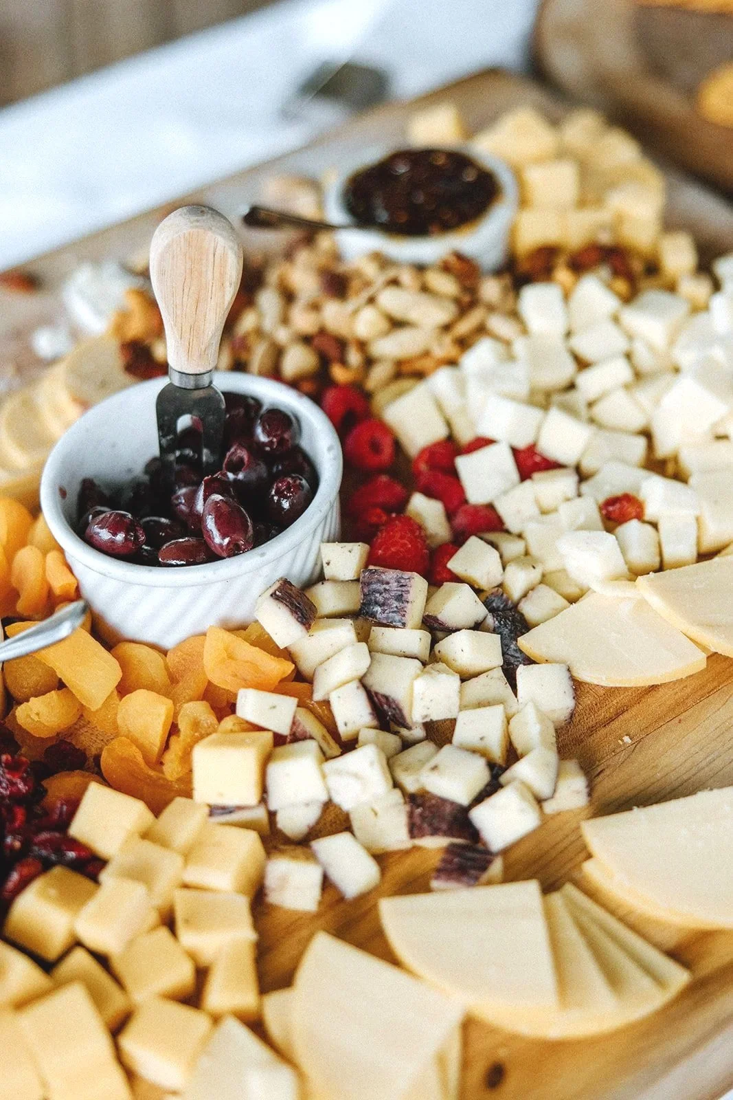 Assorted cheeses, dried cranberries, and nuts on a wooden cheese board.