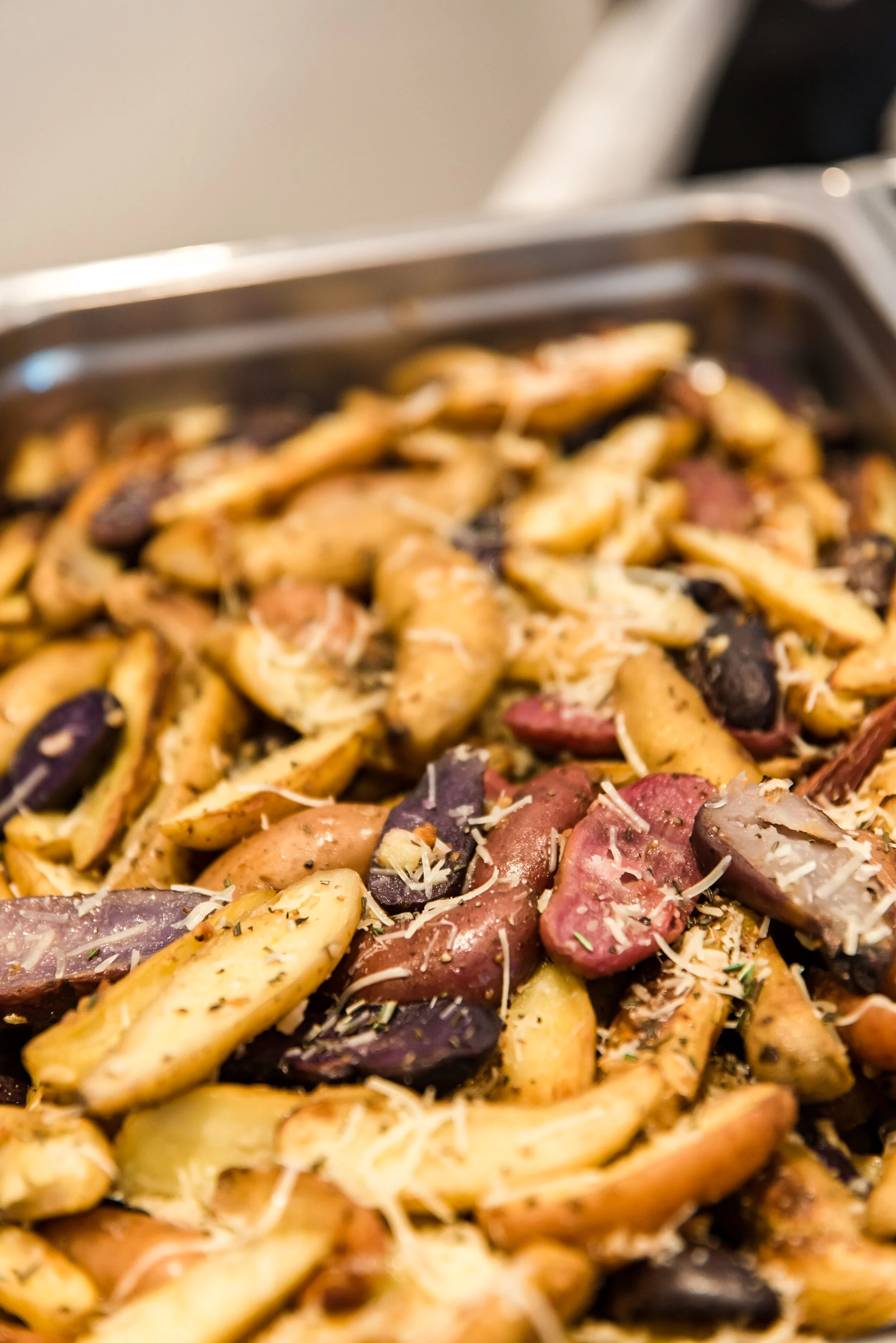 Roasted potato wedges with herbs and cheese on a baking sheet.