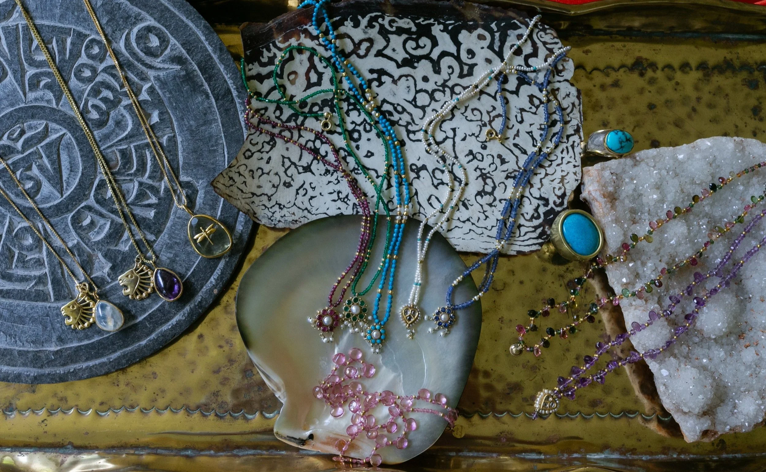 Display of colorful jewelry including necklaces, rings, and bracelets laid out on decorative stones and a metallic tray.