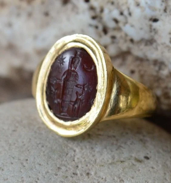 Gold signet ring with an oval red stone engraved with a building and star, resting on a stone surface.