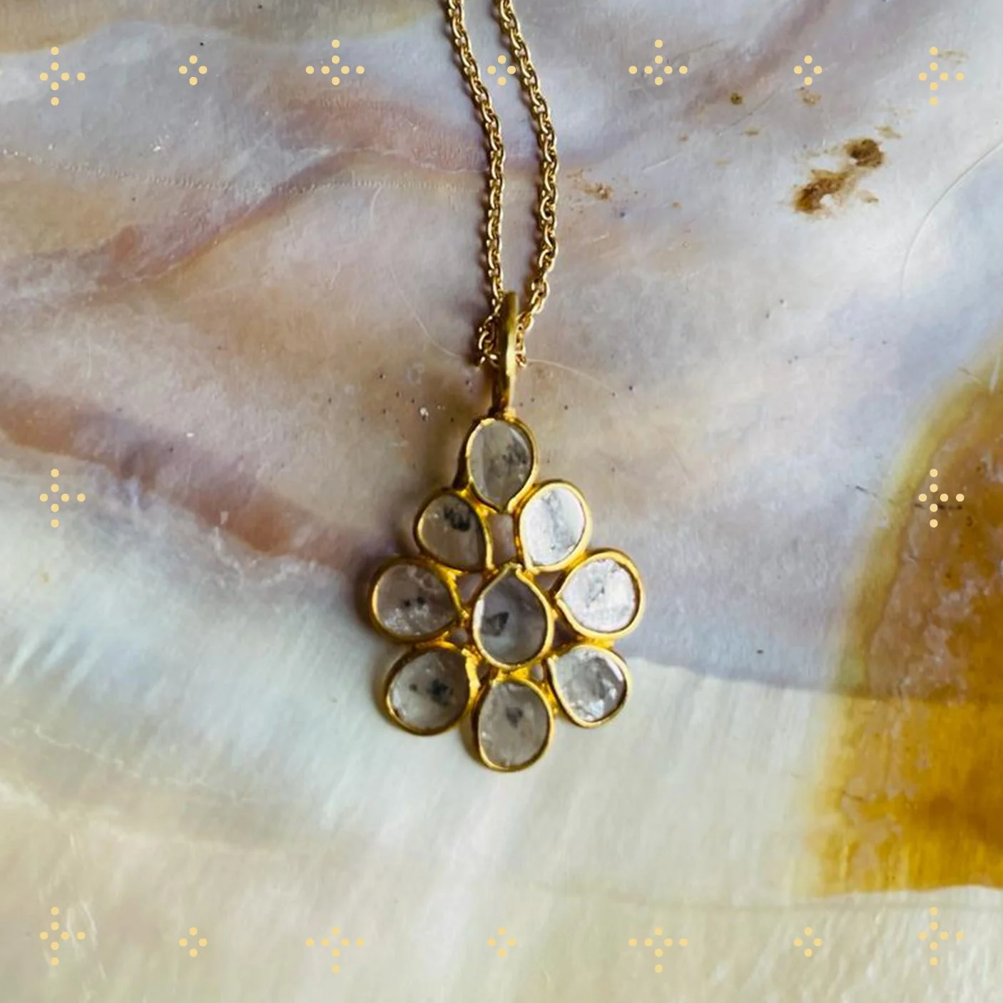 Gold necklace with a pendant of multiple oval-shaped, clear gemstones arranged in a flower-like pattern, resting on a textured, pale-colored surface.