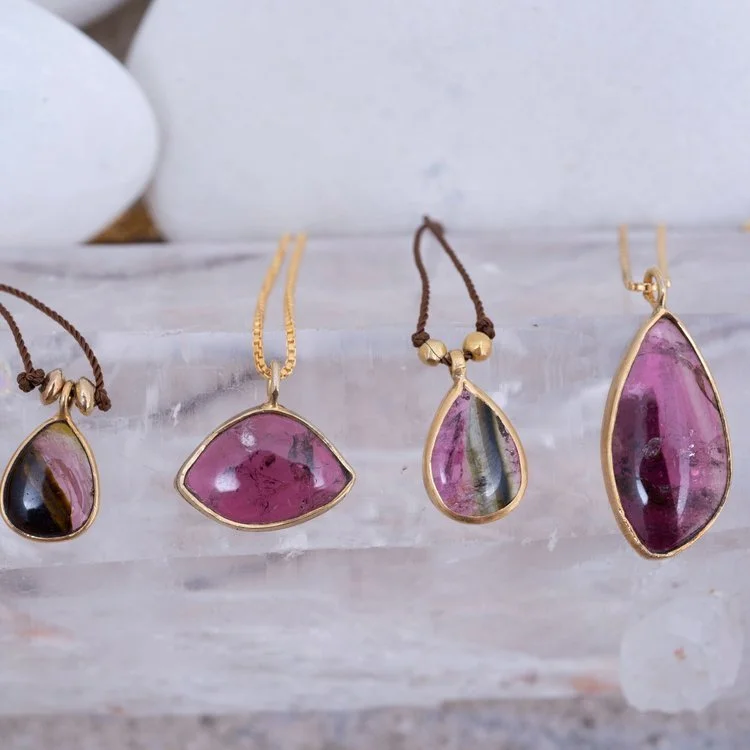 Set of four gold necklaces with pink and multicolored gemstone pendants displayed on a white stand.