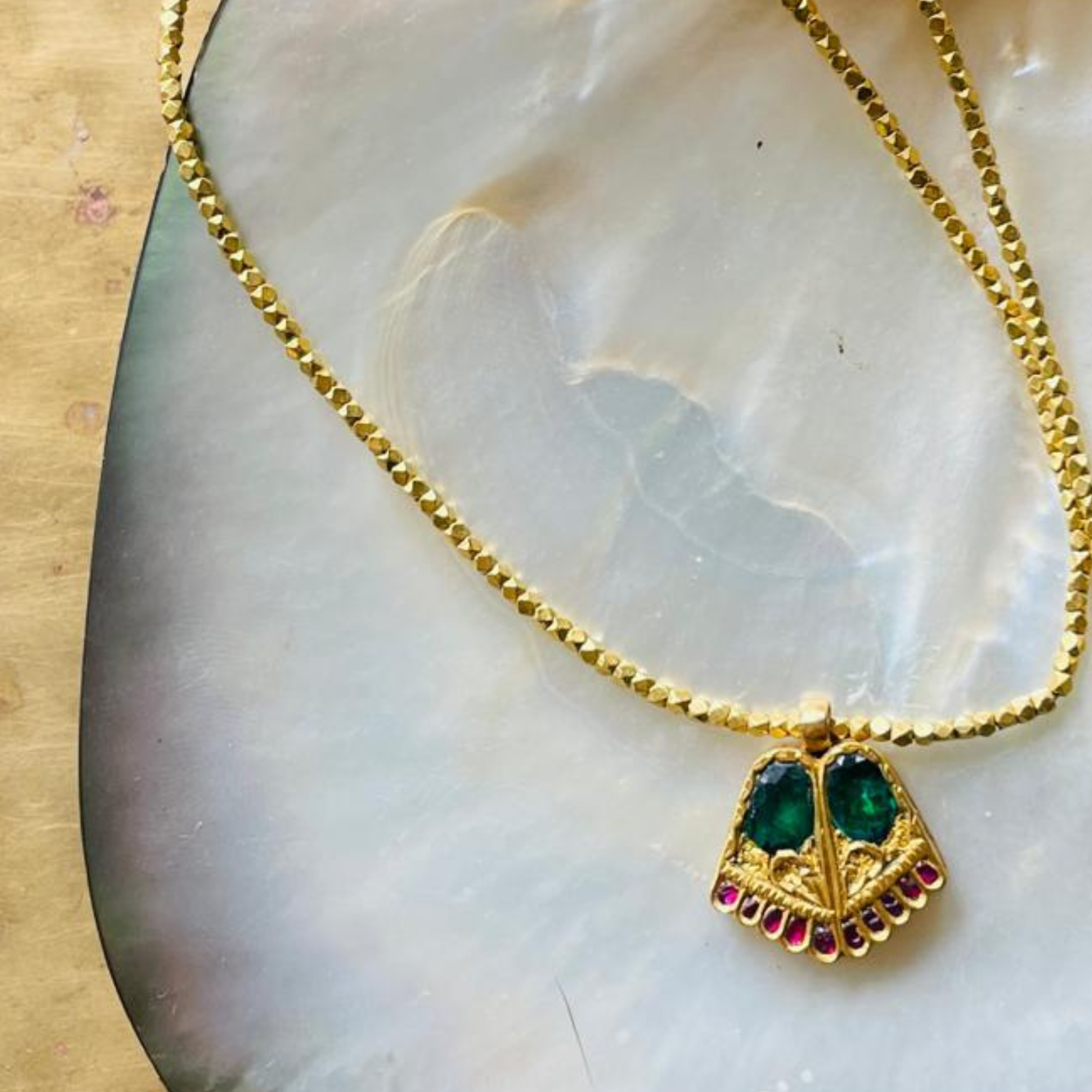 May birthstone emeralds set in gold pendant with twinkly ruby toes on gold beaded thread