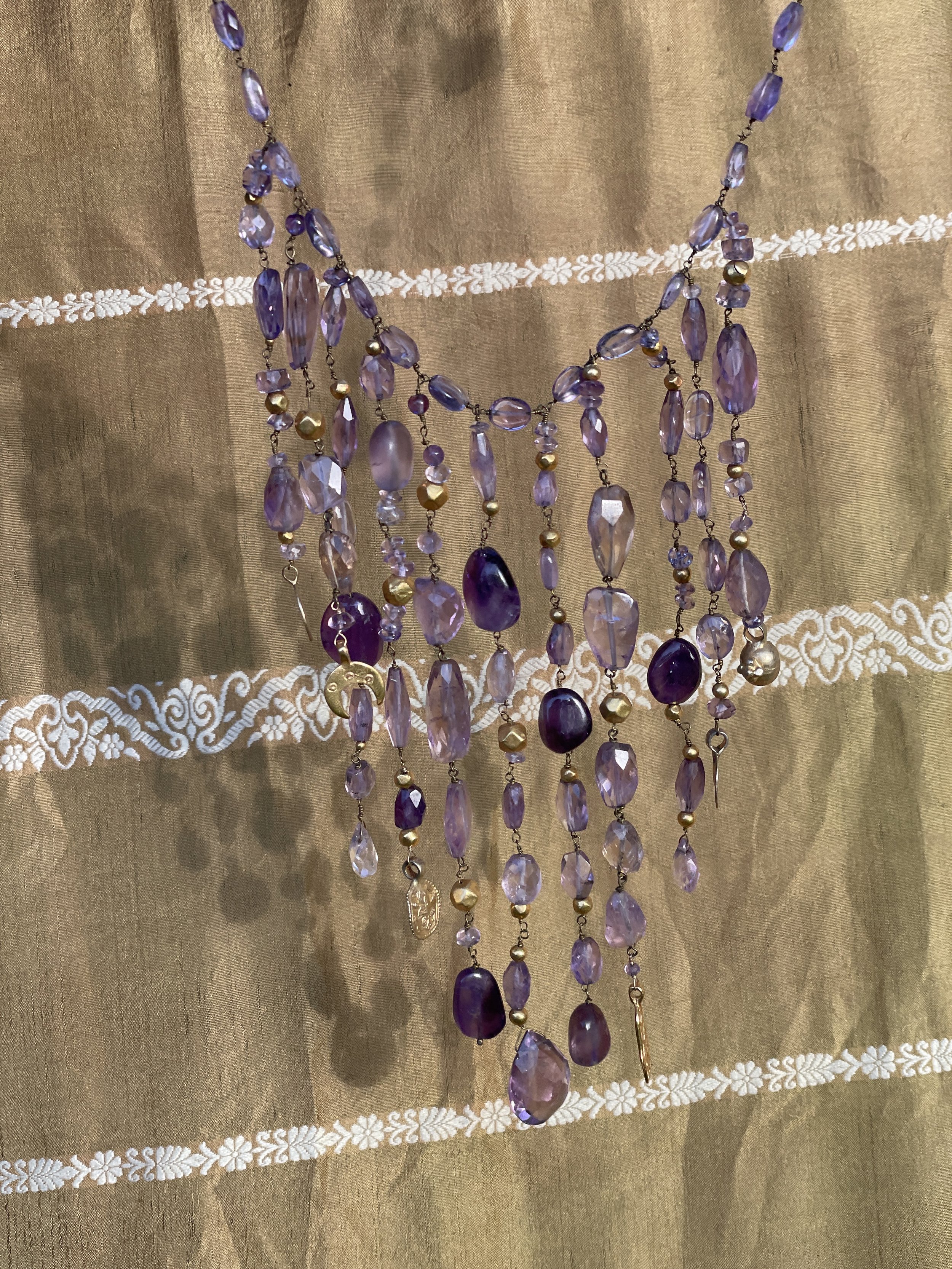 A layered purple beaded necklace with gold accents hanging against a gold fabric background.