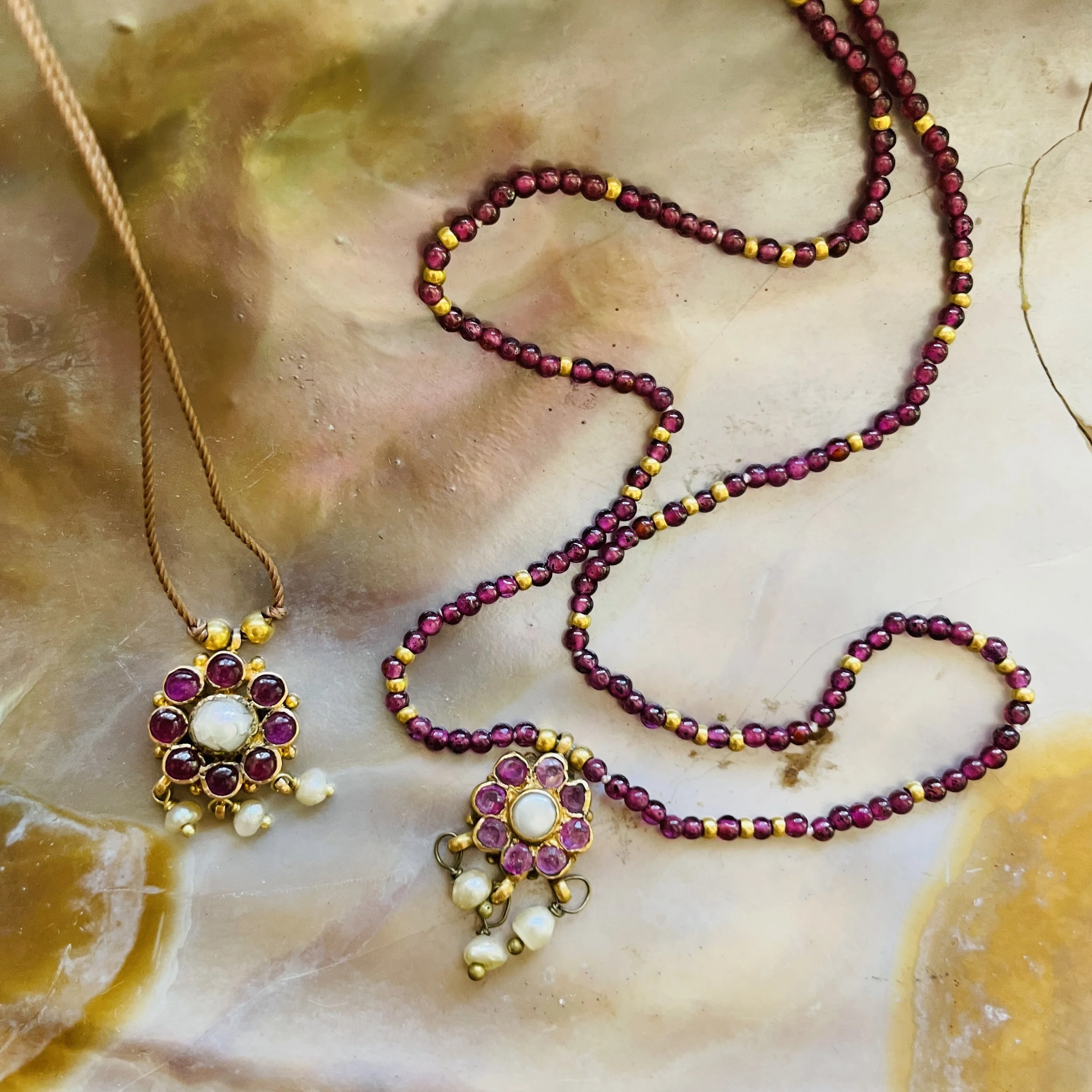 Two necklaces with purple and white beads and floral pendant designs, laid on a polished stone surface.