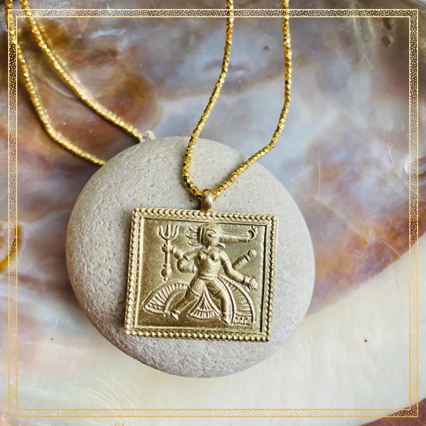 A gold pendant necklace with an engraved deity figure, resting on a round stone, with a decorative background.