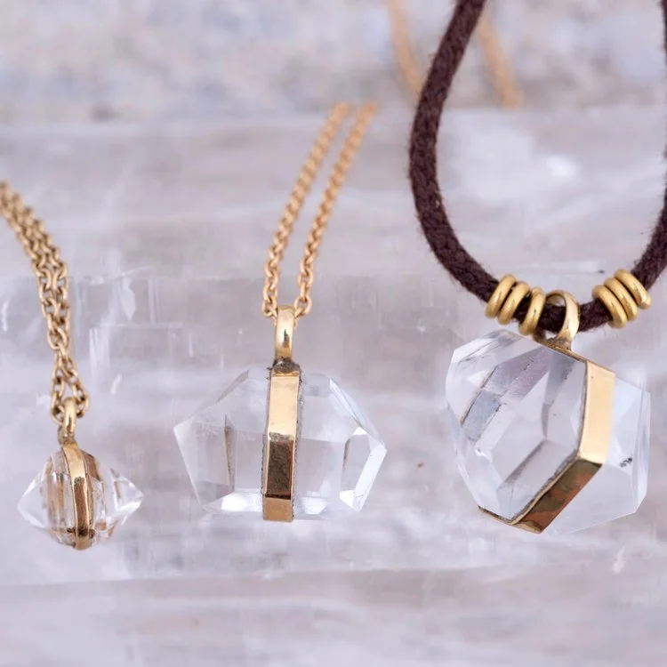 Three necklaces featuring large, clear crystal pendants with gold accents, displayed on a light-colored surface.