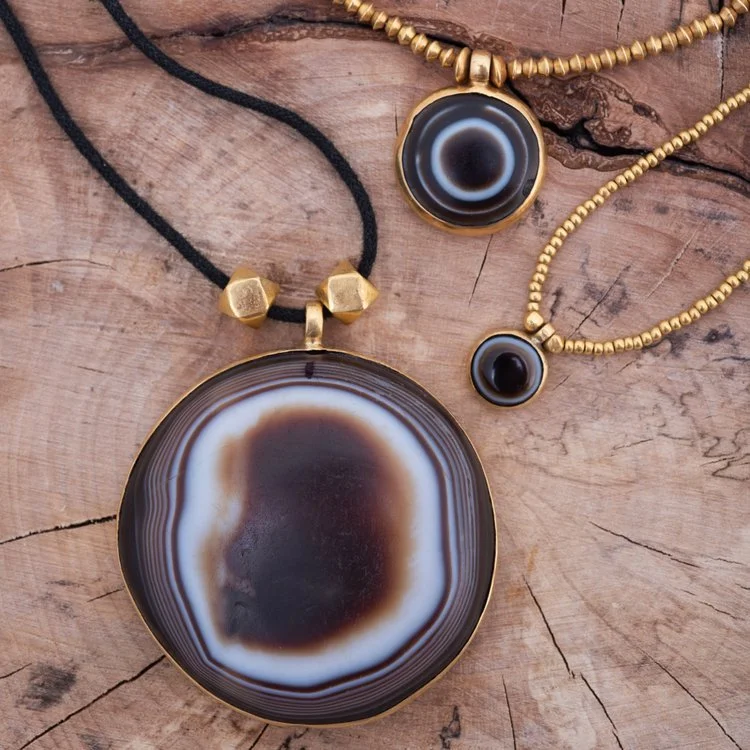 Three necklaces with large black and brown geode pendants on a wooden surface.