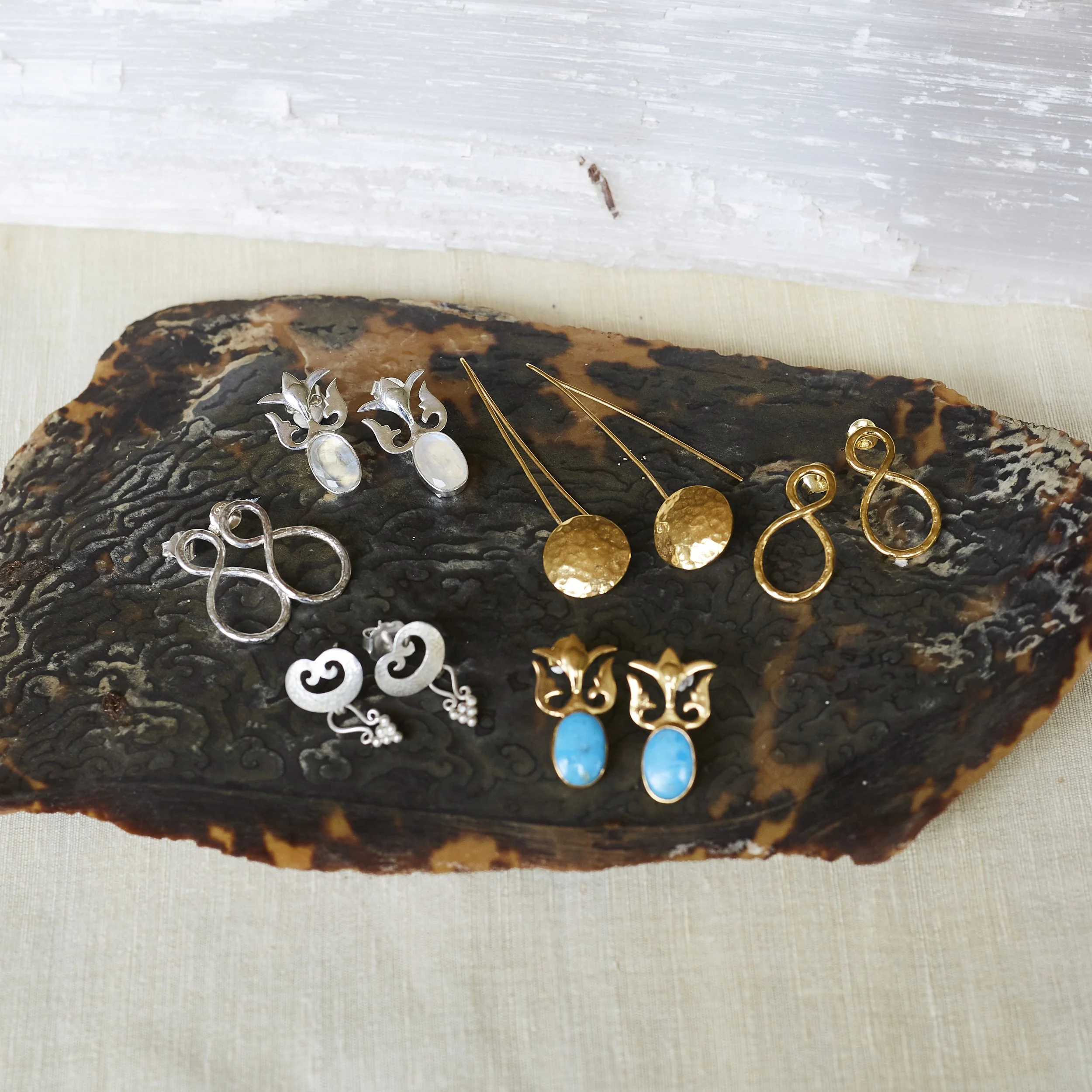 Collection of vintage-style earrings displayed on a dark, textured wooden tray.