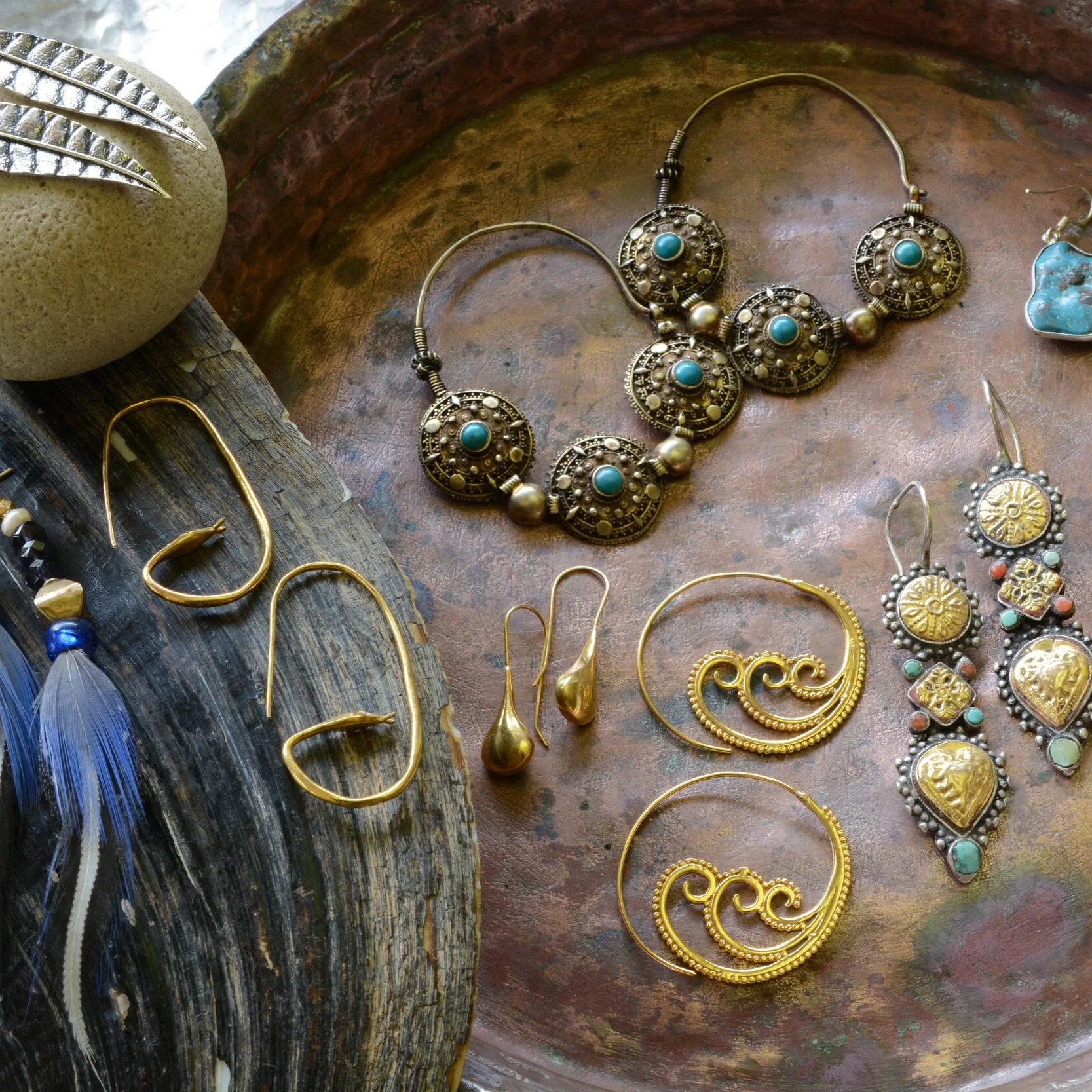 Various gold and silver jewelry including earrings, necklaces, and earrings with turquoise and coral accents displayed on a rustic surface.