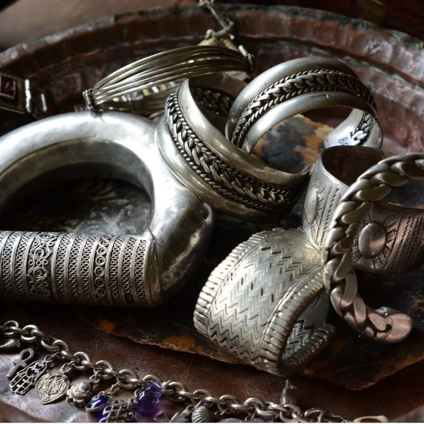 A collection of silver and metallic bangles and bracelets with intricate designs, placed on a dark wooden surface.