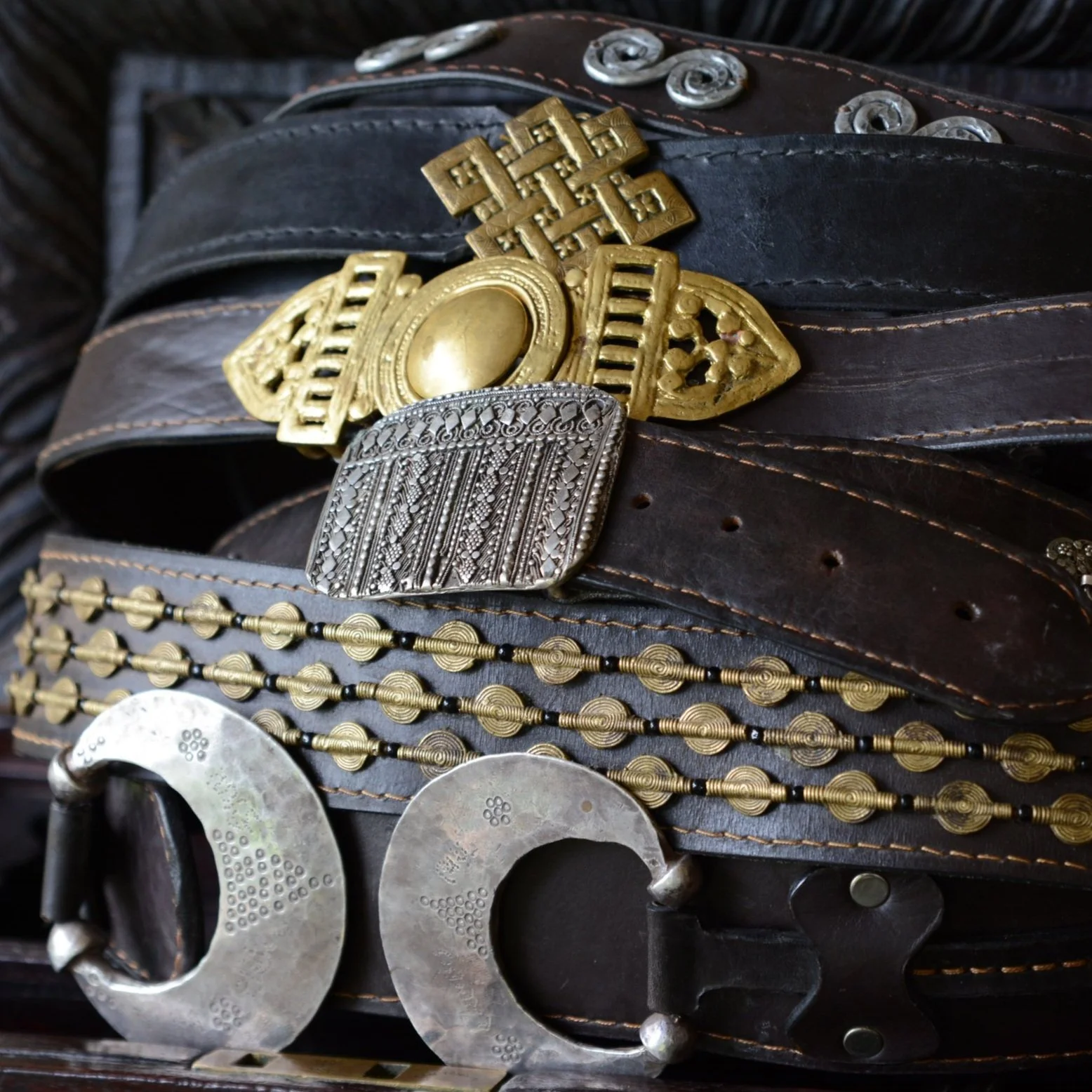 Close-up of a black leather western belt with silver and gold ornate belt buckles and decorative metal accents.