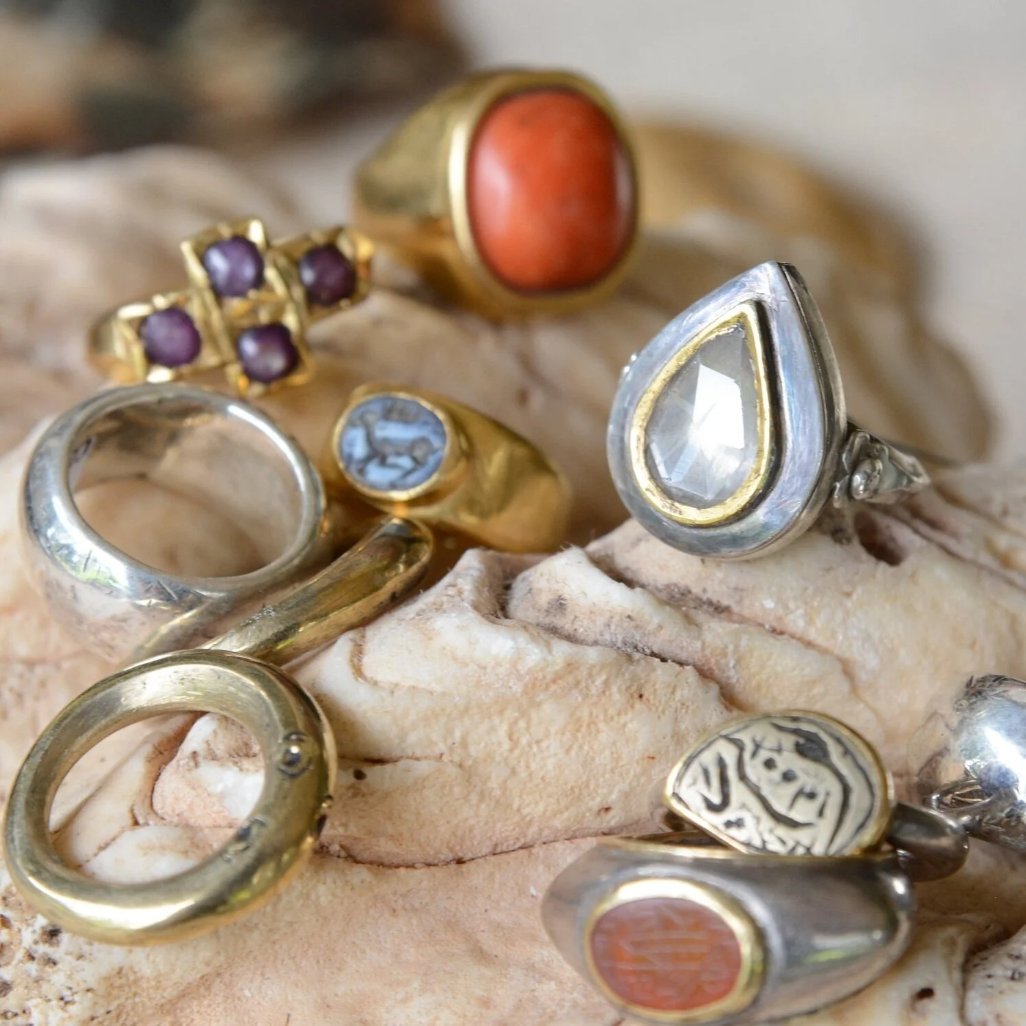 Collection of various rings with different designs and stones resting on a piece of coral.