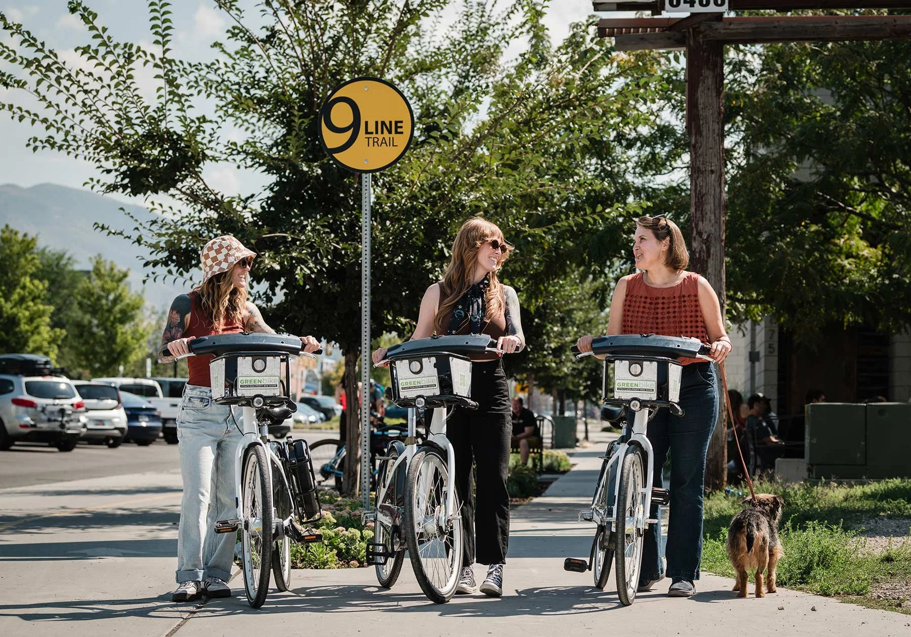 Three women stopping on their GreenBikes at a train crossing to chat