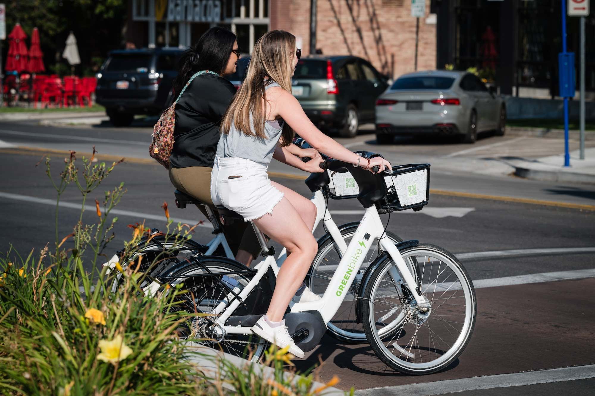 Two women friends riding GreenBikes across street