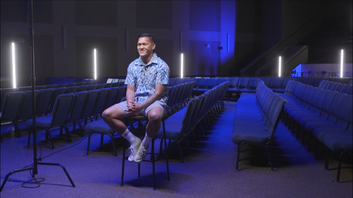 Man sitting on a chair in an empty auditorium with blue lighting and rows of chairs.