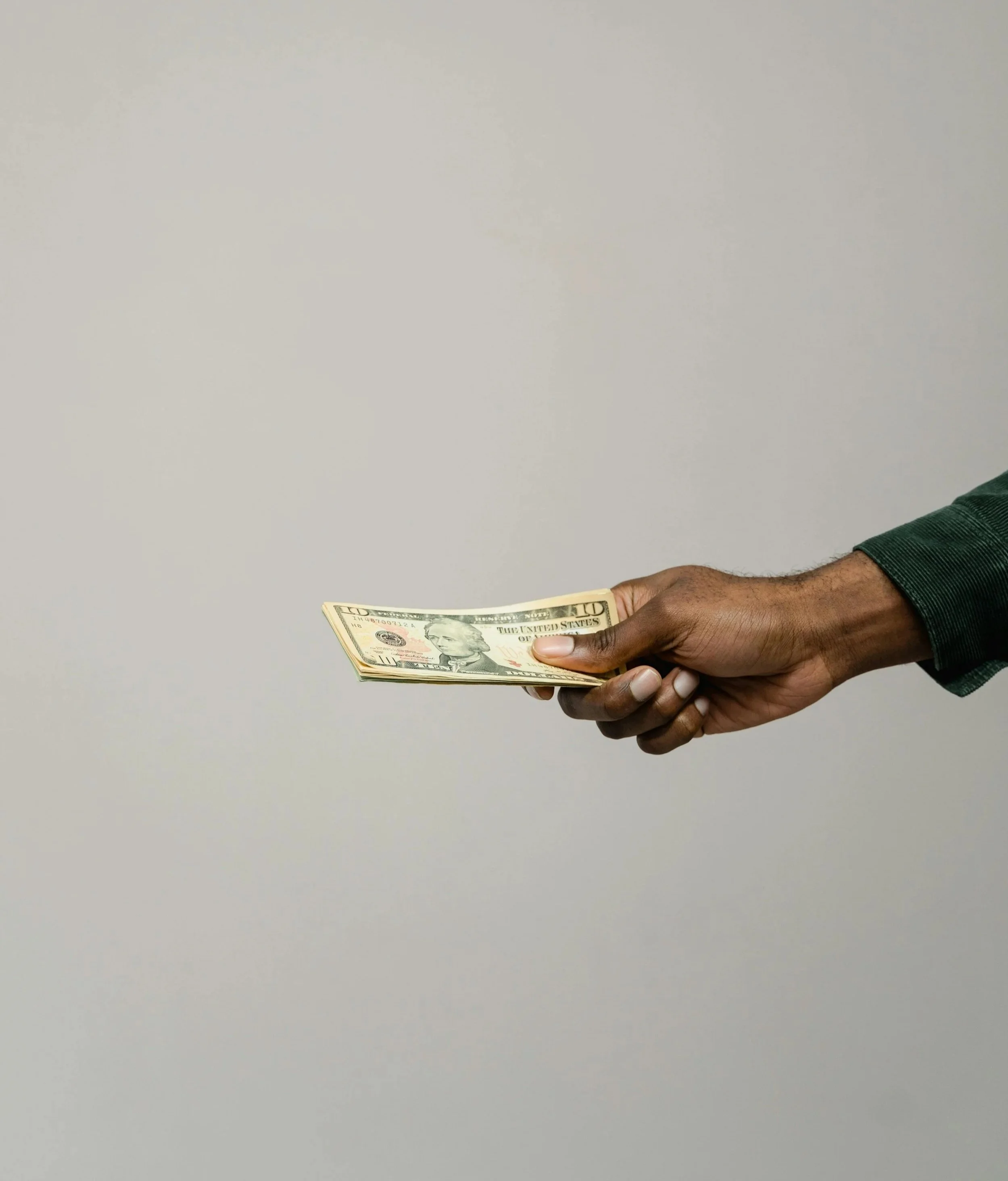 Main qui tient des billets de dix dollars américains contre un fond gris clair.