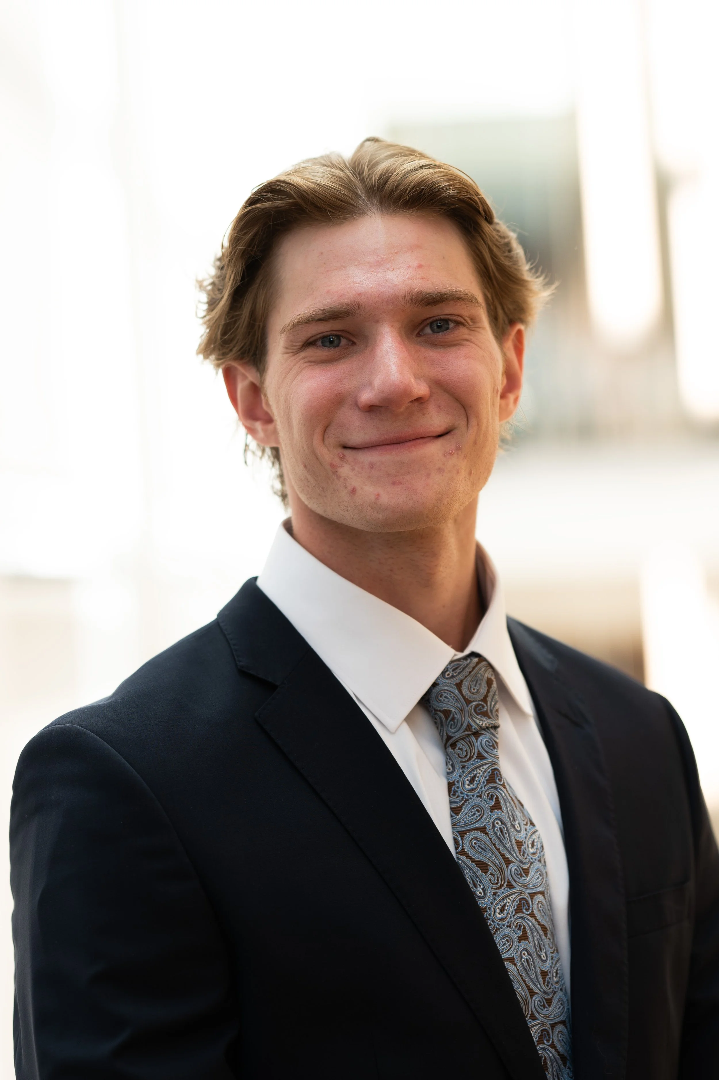 Young man in a suit and tie smiling in a professional setting.