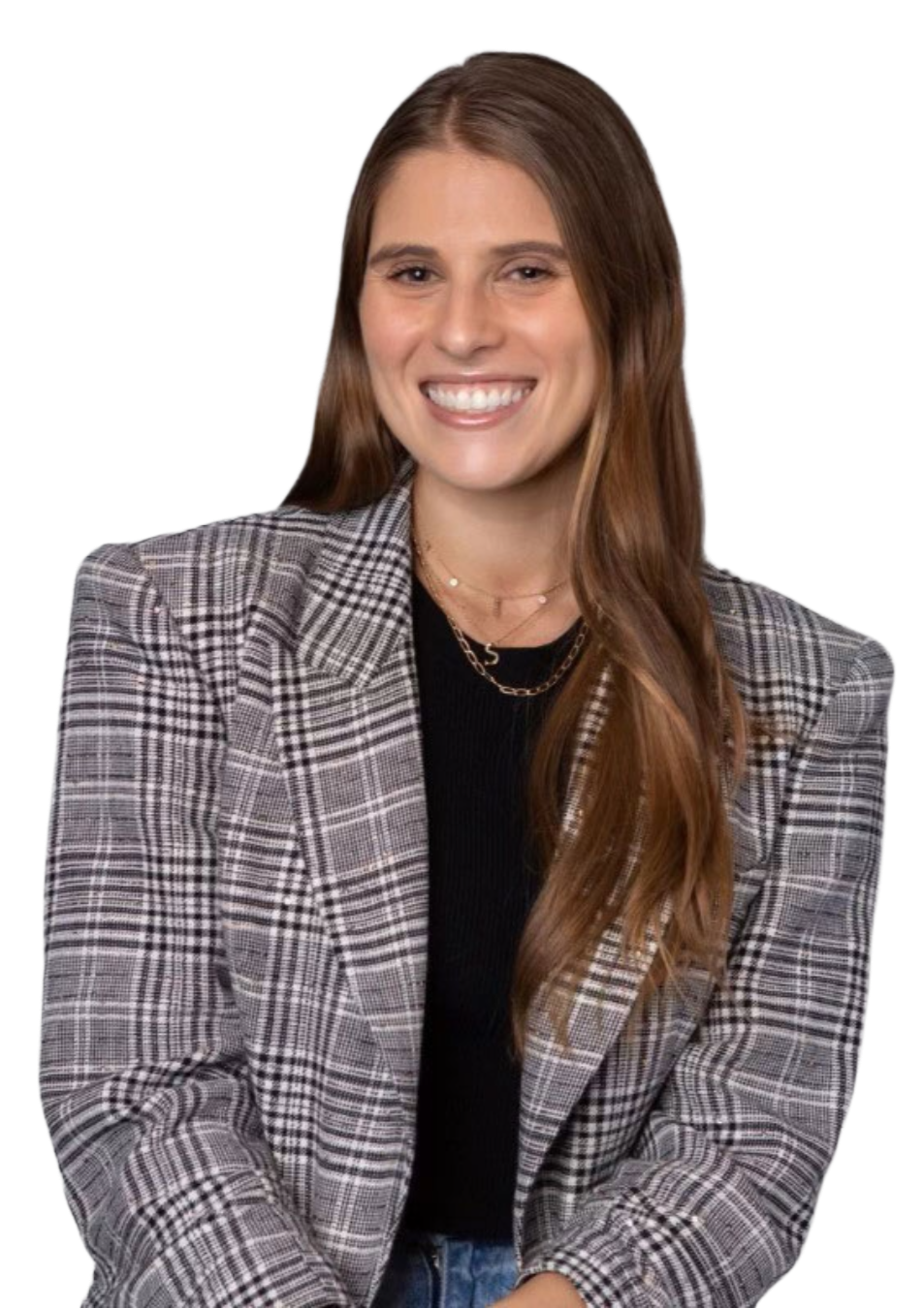 A smiling woman with long brown hair, wearing a plaid blazer, black top, layered gold necklaces, and blue jeans.