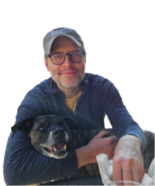 A man with glasses and a cap smiling while holding a black dog