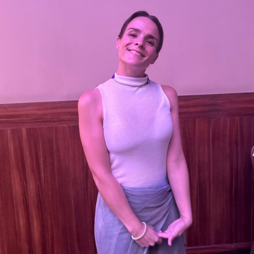Mujer sonriendo con ropa sin mangas en un entorno con paredes rosadas y madera.