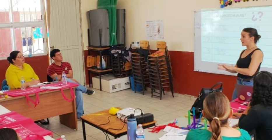 Montse explicando a un grupo de docentes en un aula, la importancia de los apoyos visuales de comunicación en el aula de clases y aclarando dudas de los docentes.