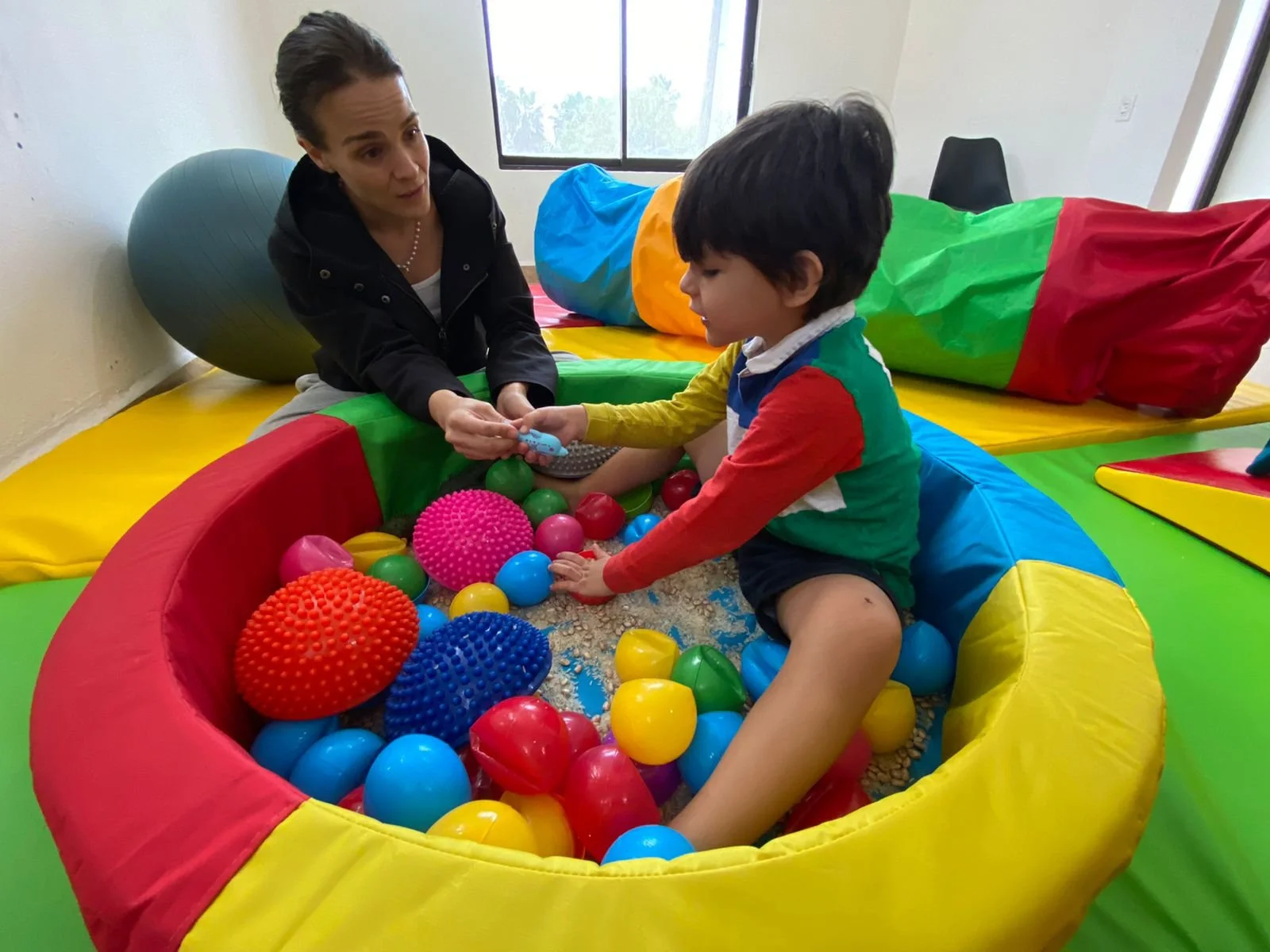 Niño jugando en una piscina de pelotas y otros materiales sensoriales con Montse.