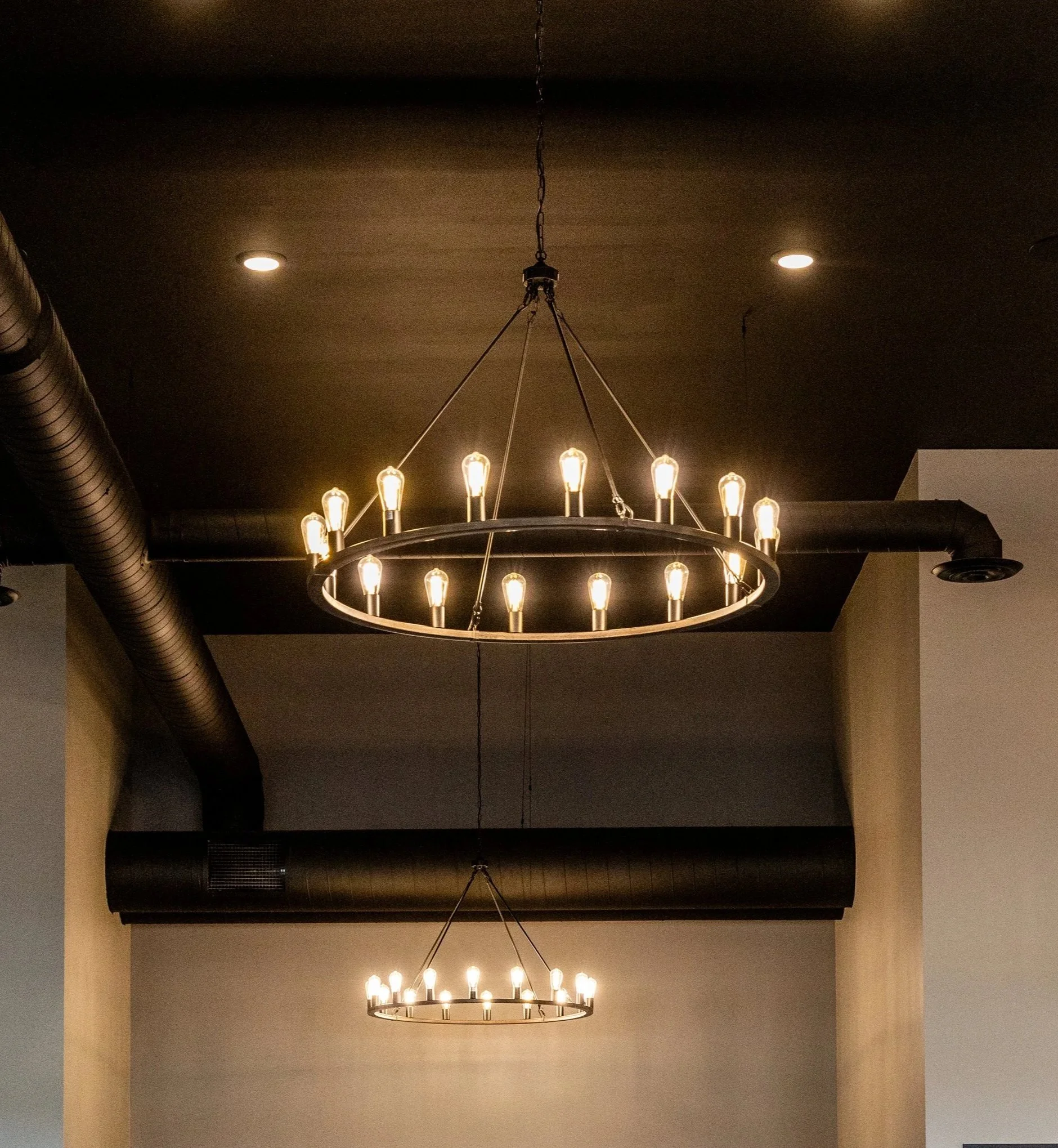 Two circular chandelier light fixtures hanging from a black ceiling in an indoor space.