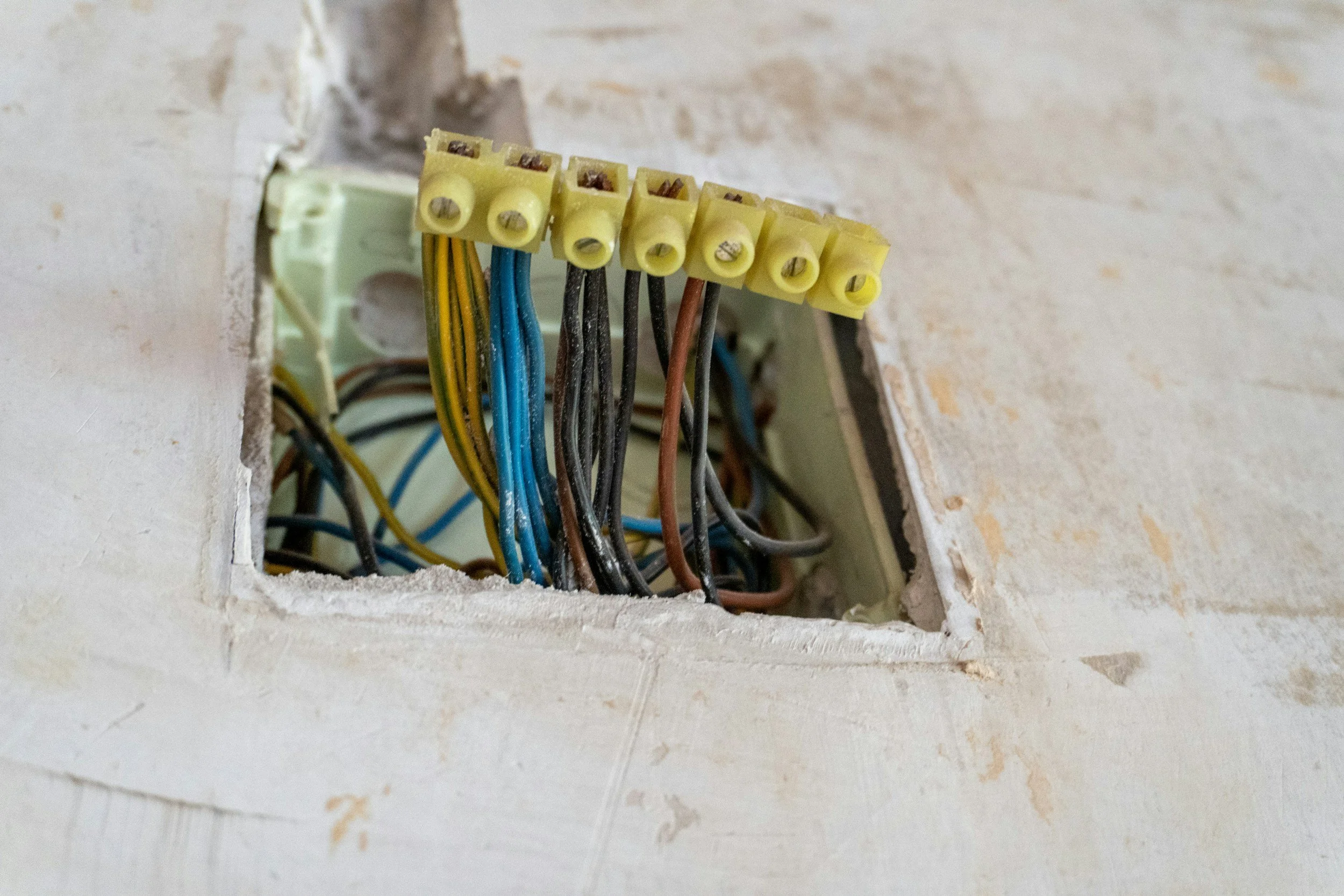 An open electrical wall box with multiple colored wires and a yellow terminal block inside.