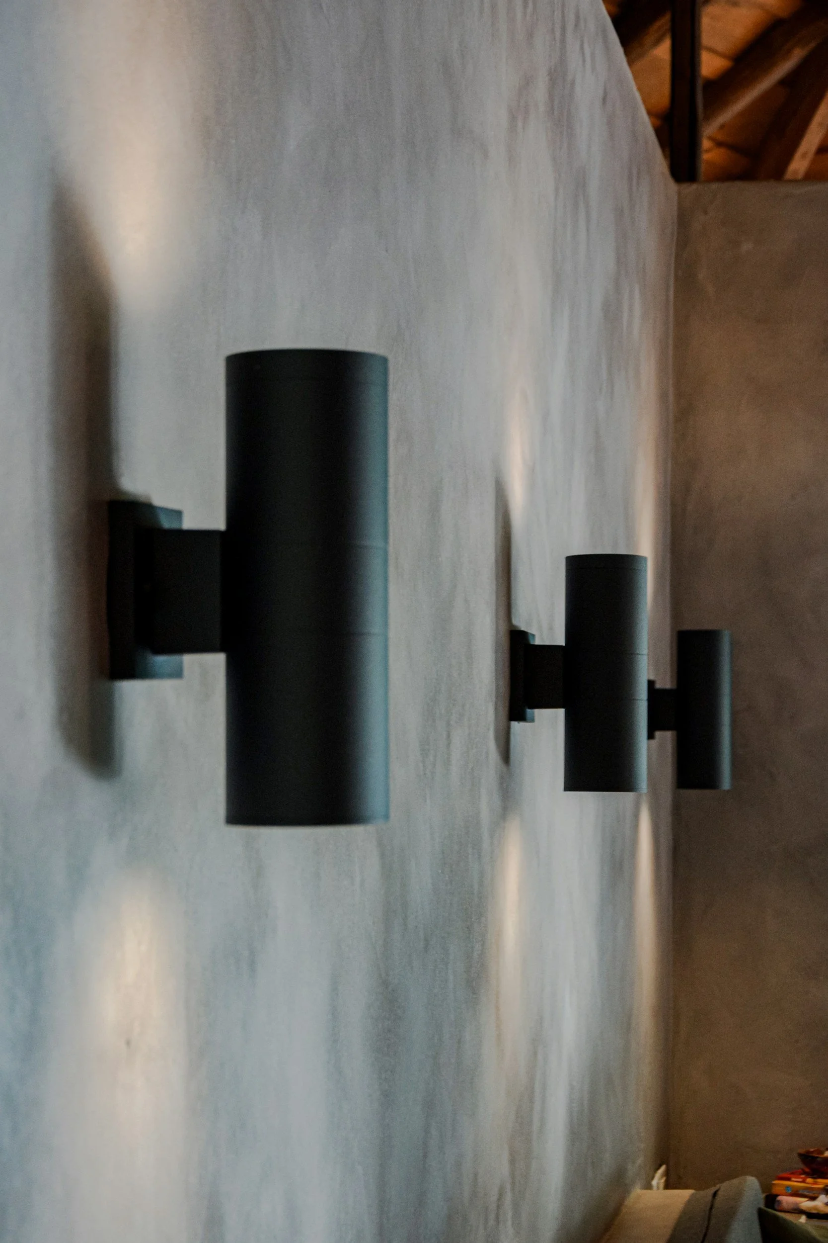 Three black cylindrical wall sconces casting light on a grey textured wall.