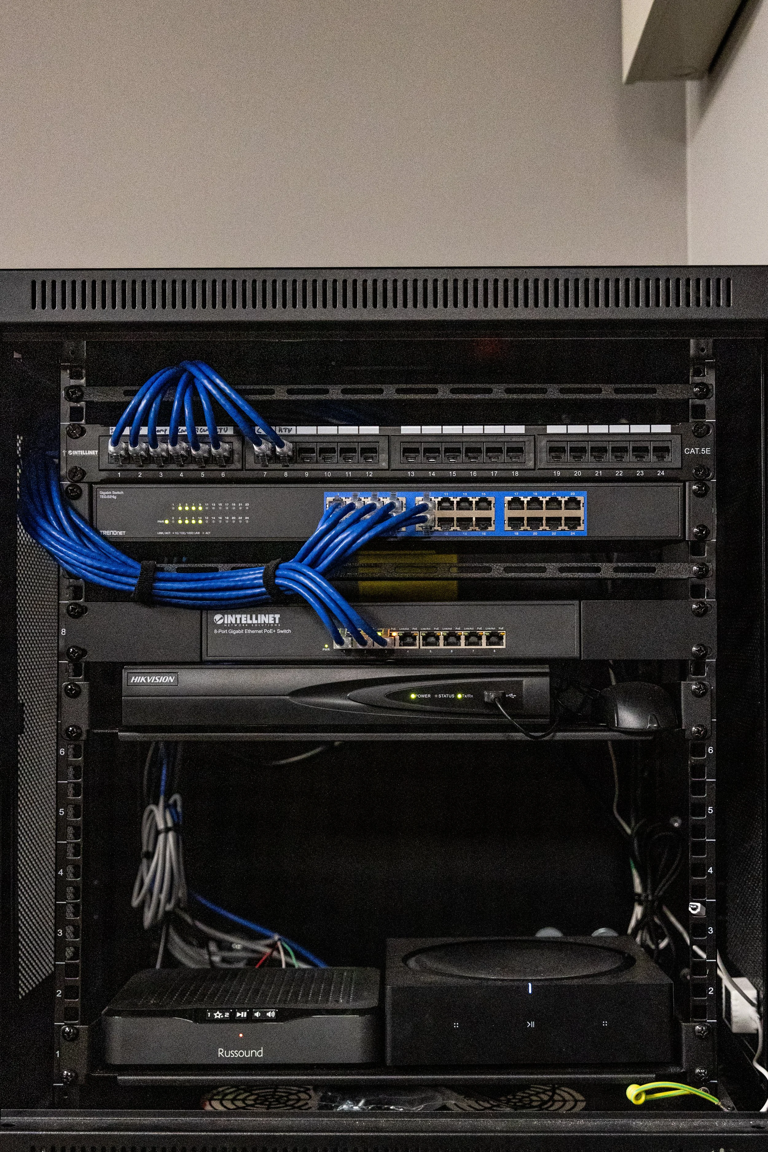 Network server rack with switches, patch panels, a Hikvision device, a Russound audio system, and connected cables.