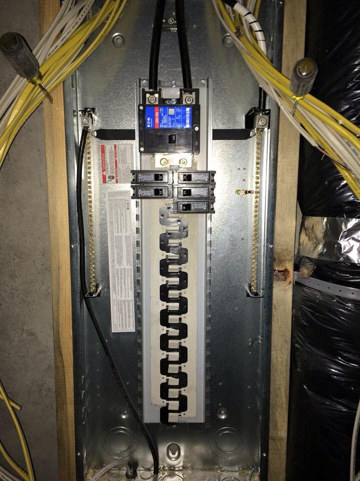 An electrical panel with circuit breakers and yellow wiring mounted on a wooden board.