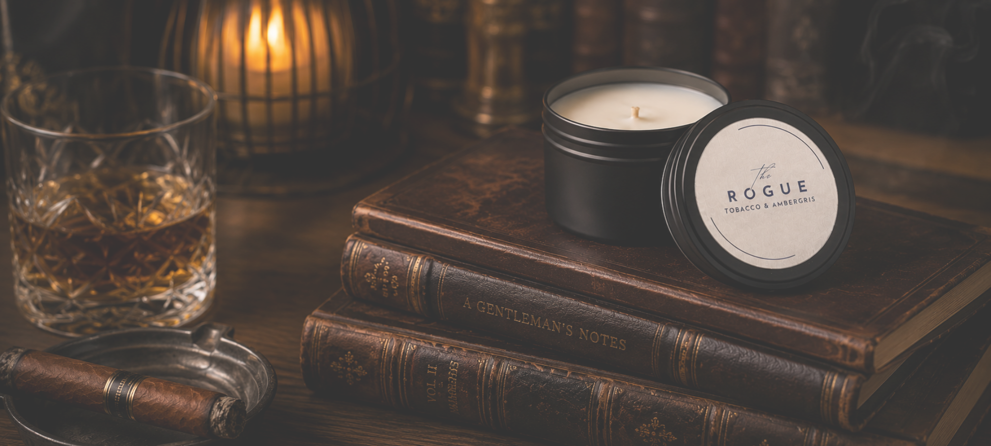 The Rogue Tobacco & Amber Candle by Coconuts & Conrbread Candle Co. Matte black tin with a silver label sitting on top of worn leather books