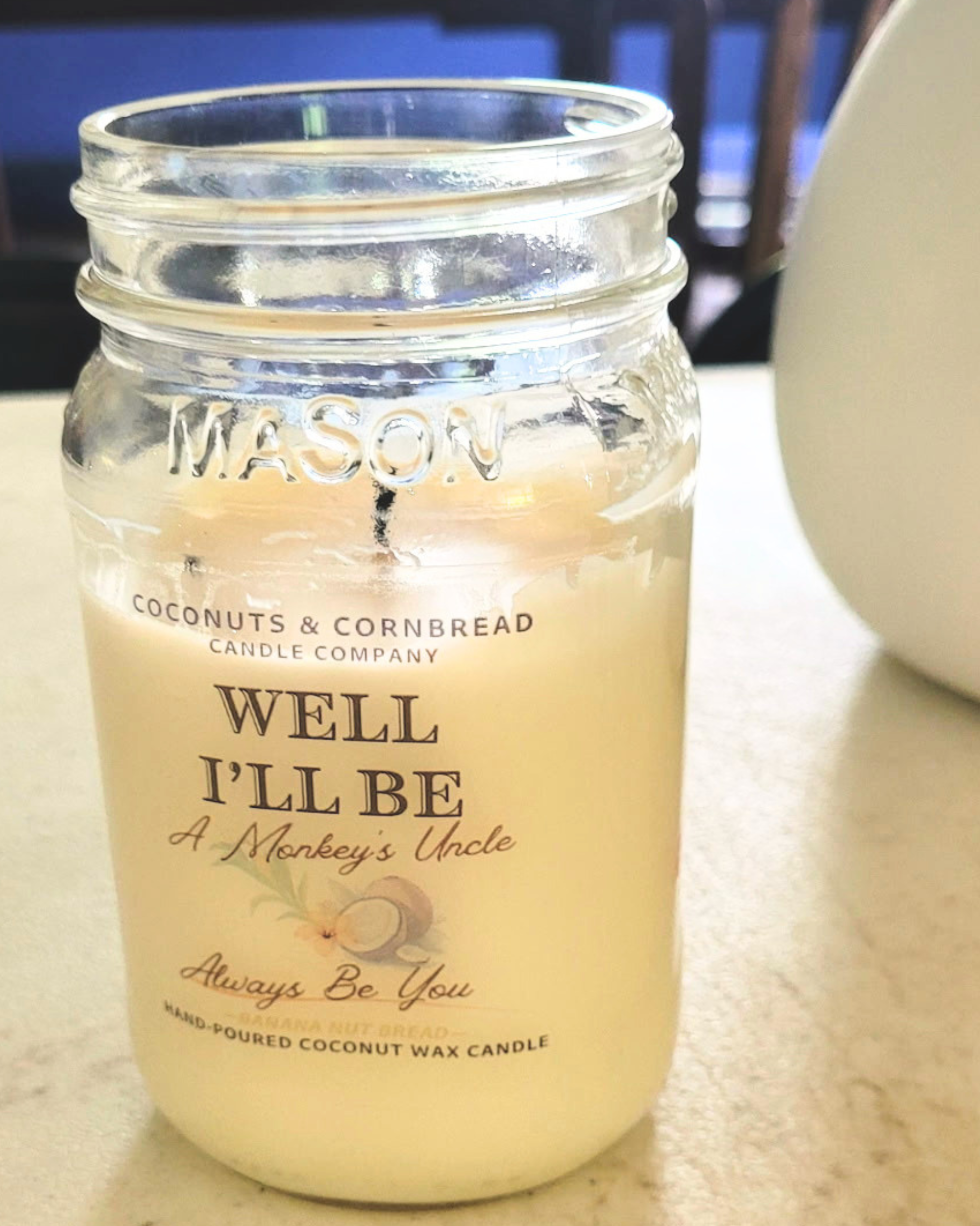 A candle jar with a label that reads 'WELL, I'LL BE', 'A Monkey's Uncle', banana nut bread scent made by coconuts and cornbread candle company