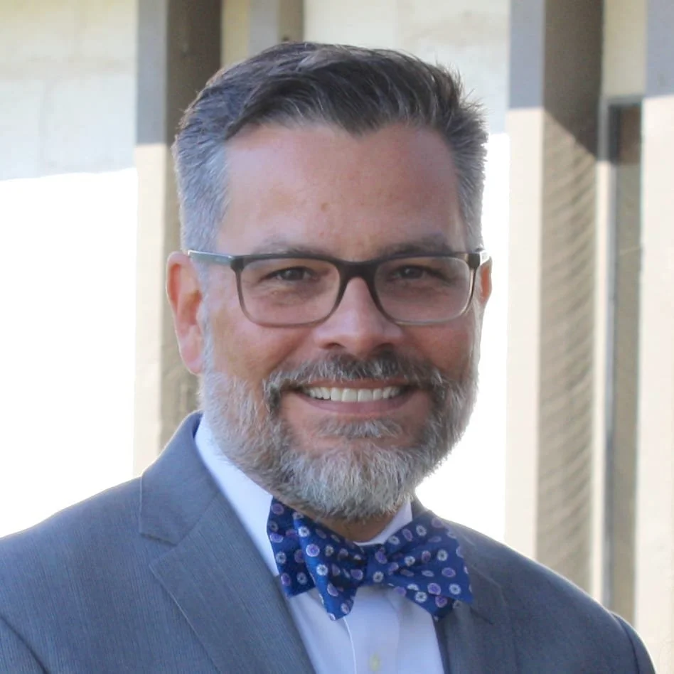 A photo of Mitch smiling in a suit with a bowtie.