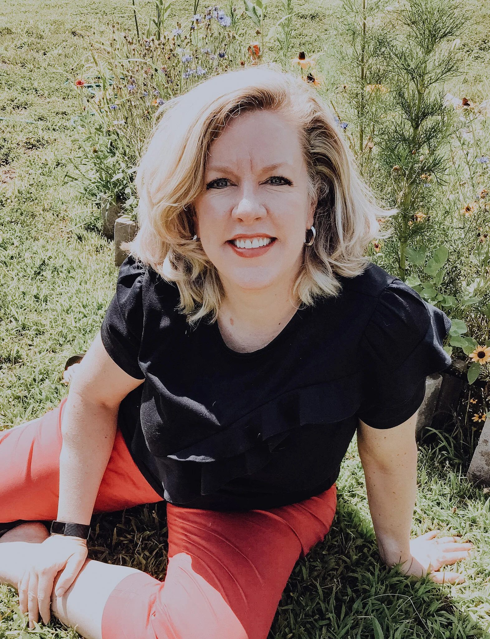 A photo of Rev. Donna smiling up at the camera while sitting on the ground.