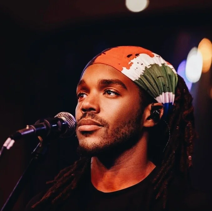 A photo of Art looking into the crowd while standing on stage in front of a microphobne.