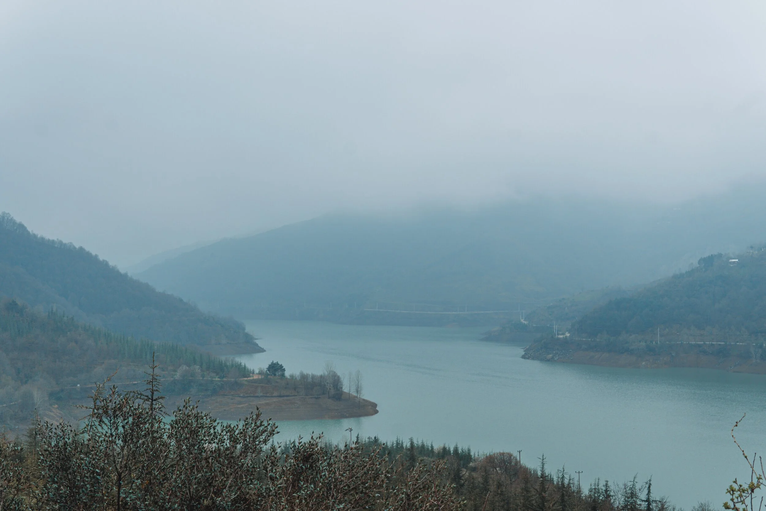 A photo of a lake in the fog between mountains.