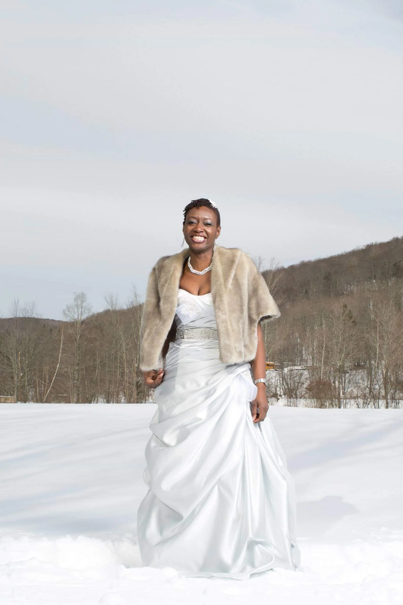 A photo of Bukola in her wedding dress, standing in a snowy field with a hillside in the background. She is wrapped in a fur shawl.