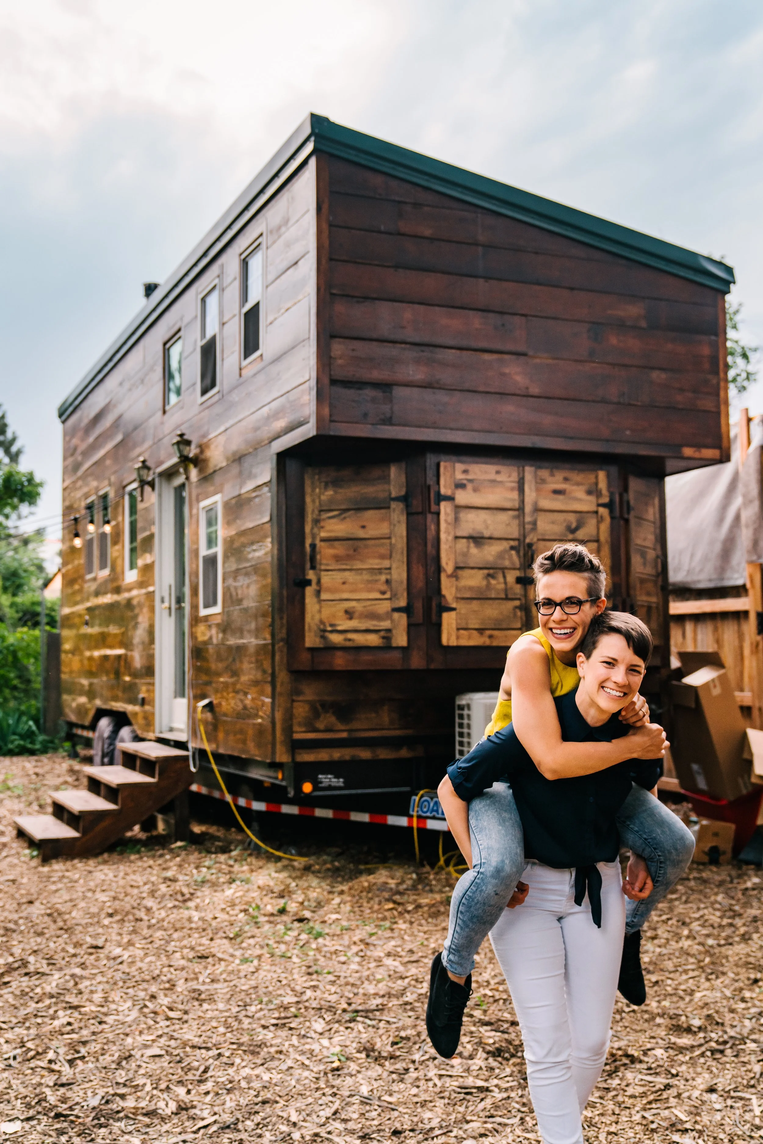 A photo of Carmen and their partner in front of a tiny house.