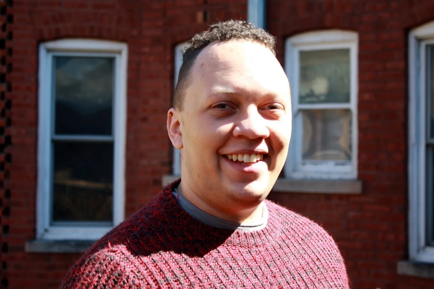 A photo of Carter in a red sweater standing in front of a building's red brick wall.